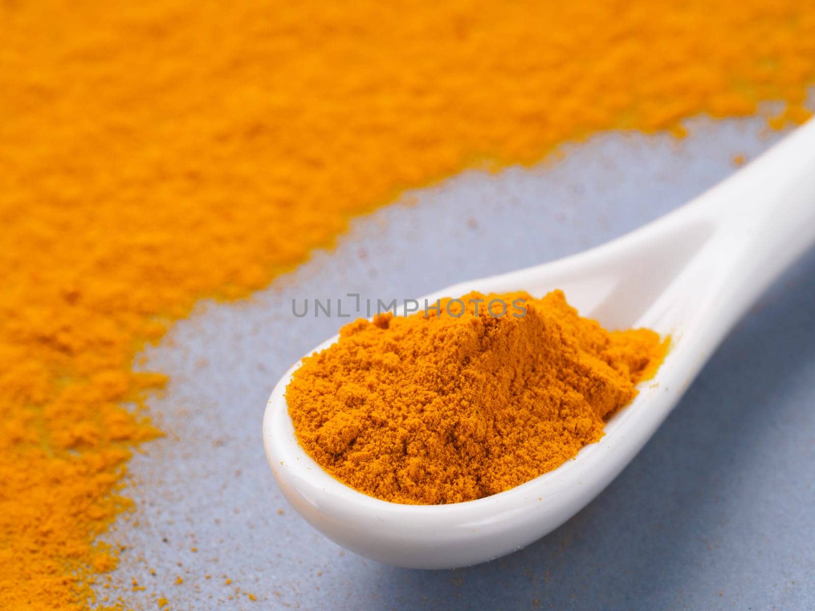 Turmeric Powder or Curcuma longa and white spoon with turmeric powder on gray background. Copy space for text.