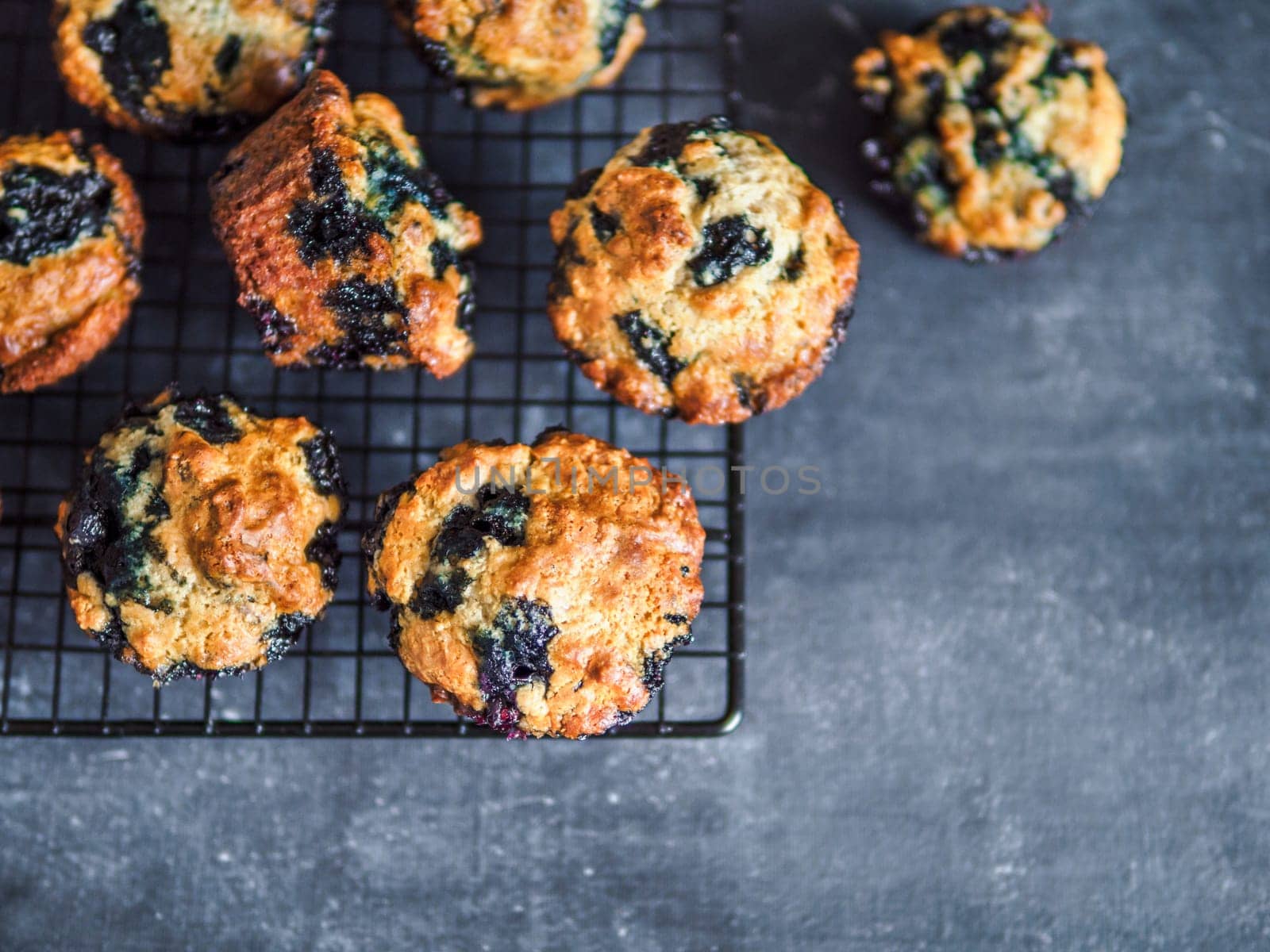 Homemade vegan blueberry muffins on cooling rack. Vegetarian egg-free muffins on dark background. Top view or flat lay. Copy space for text or design.