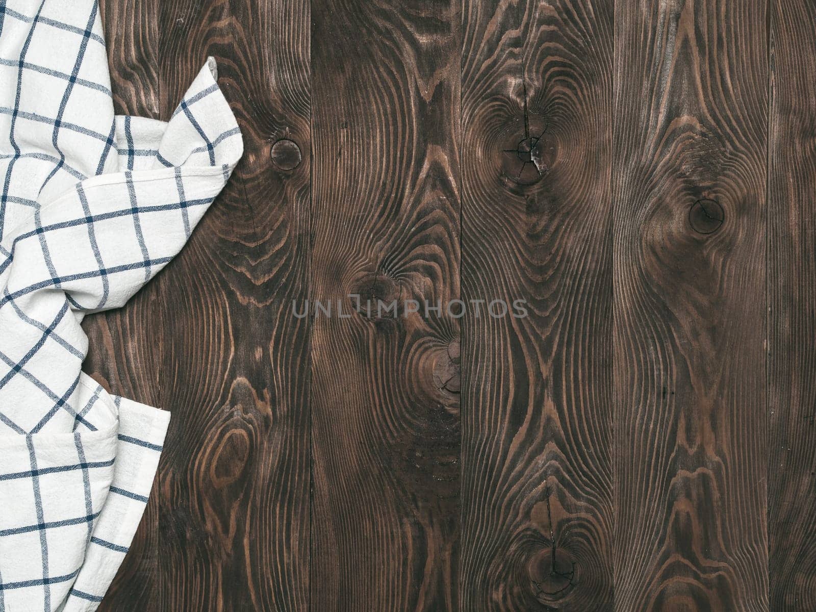 View from above on brown wooden table with linen kitchen towel or textile napkin. Blue tablecloth on dark brown wood tabletop. Copy space for text. Can use as mock up for design