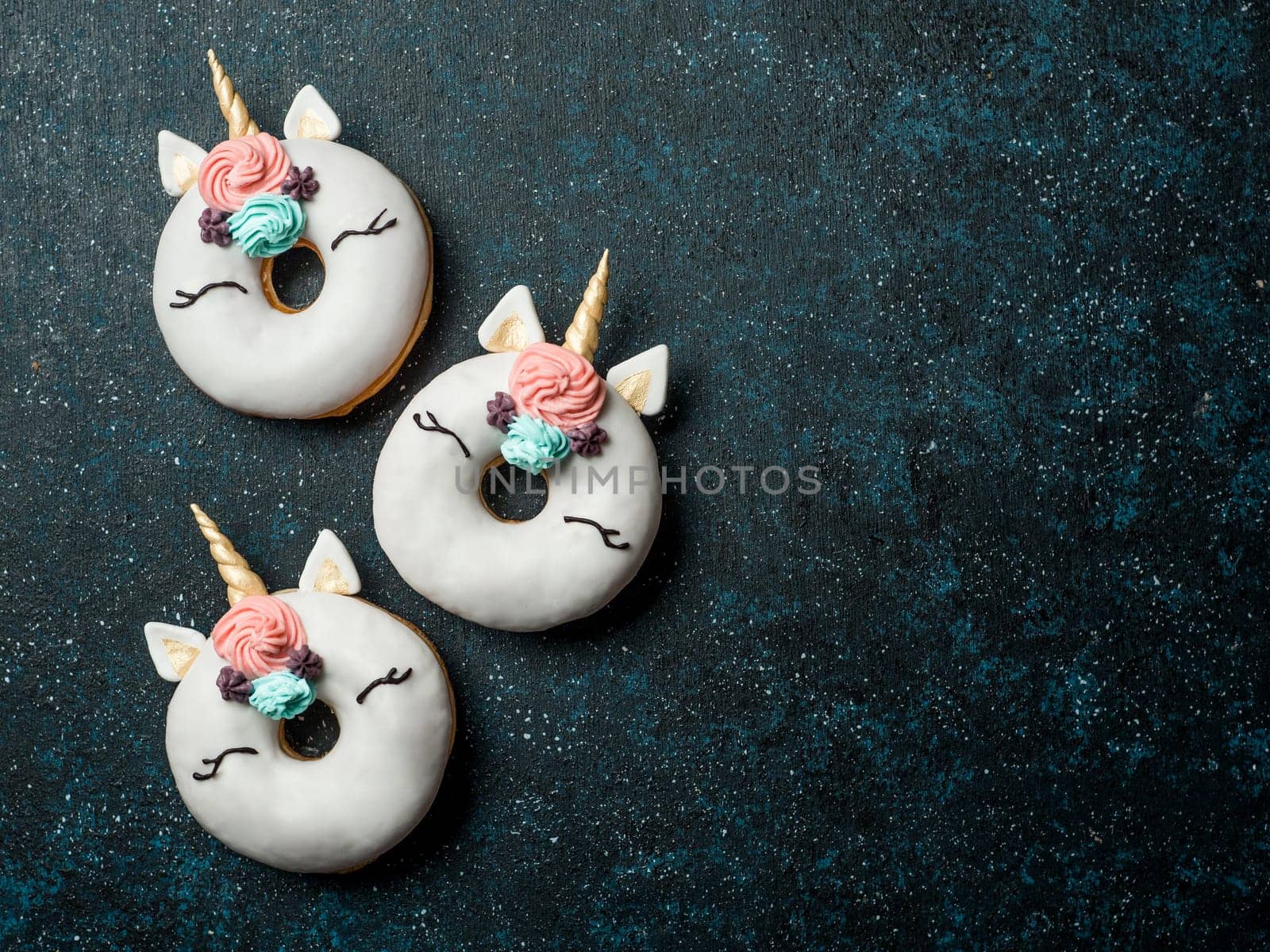 Unicorn donuts over dark background. Trendy donut unicorn with white glaze. Top view or flat lay. Copy space for text.