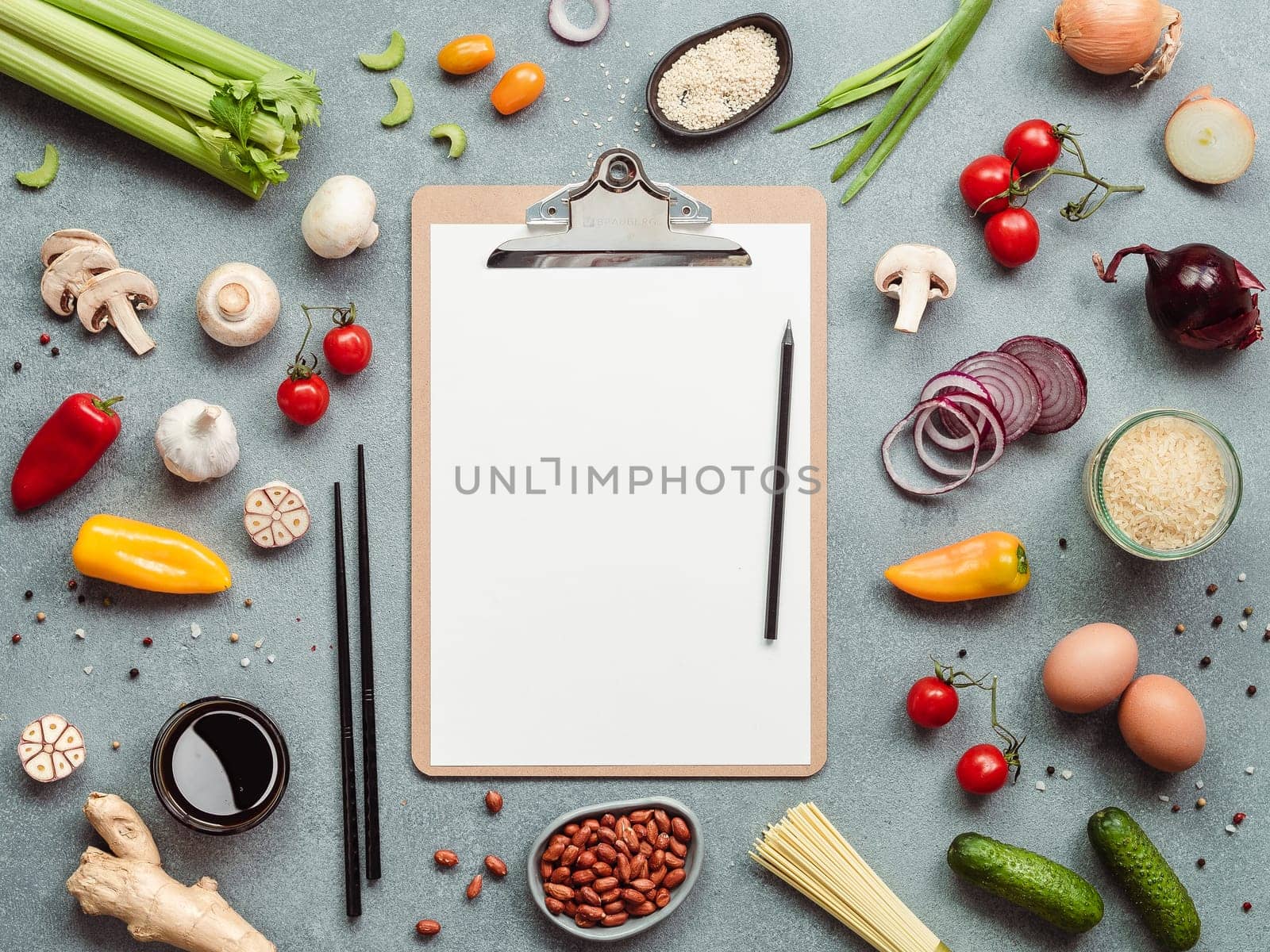 Asian ingredients and clipboard with white paper sheet. Various of Chinese cooking ingredients and chopsticks on gray stone background. Asian food concept. Copy space for text. Top view or flat lay.