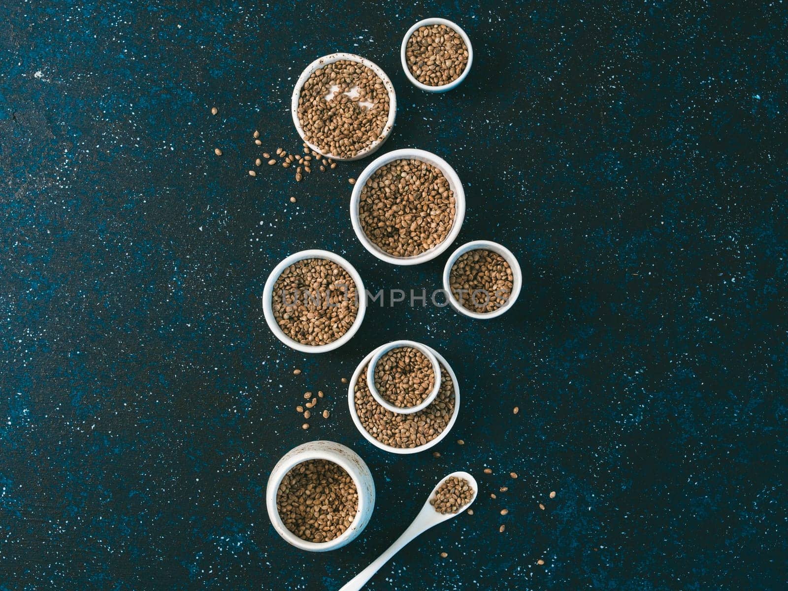 Hemp seeds in small white bowls and spoon on dark blue tabletop. Set of small bowls with raw organic unrefined hemp seed. Superfood and vegan concept. Top view or flat lay.Copy space for text.
