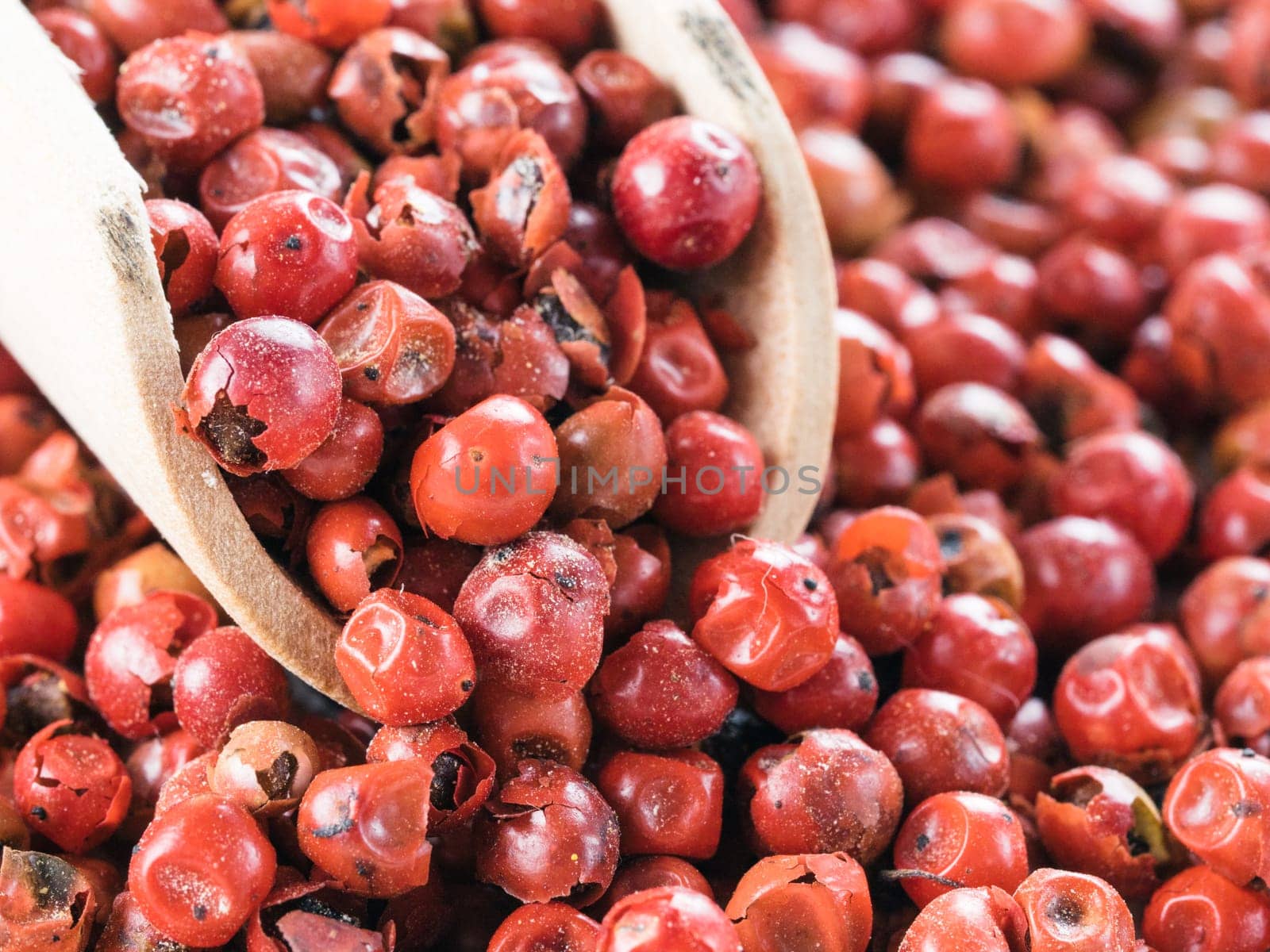 Wooden scoop filled with dried pink pepper berries. Close up view of pink peppercorn.