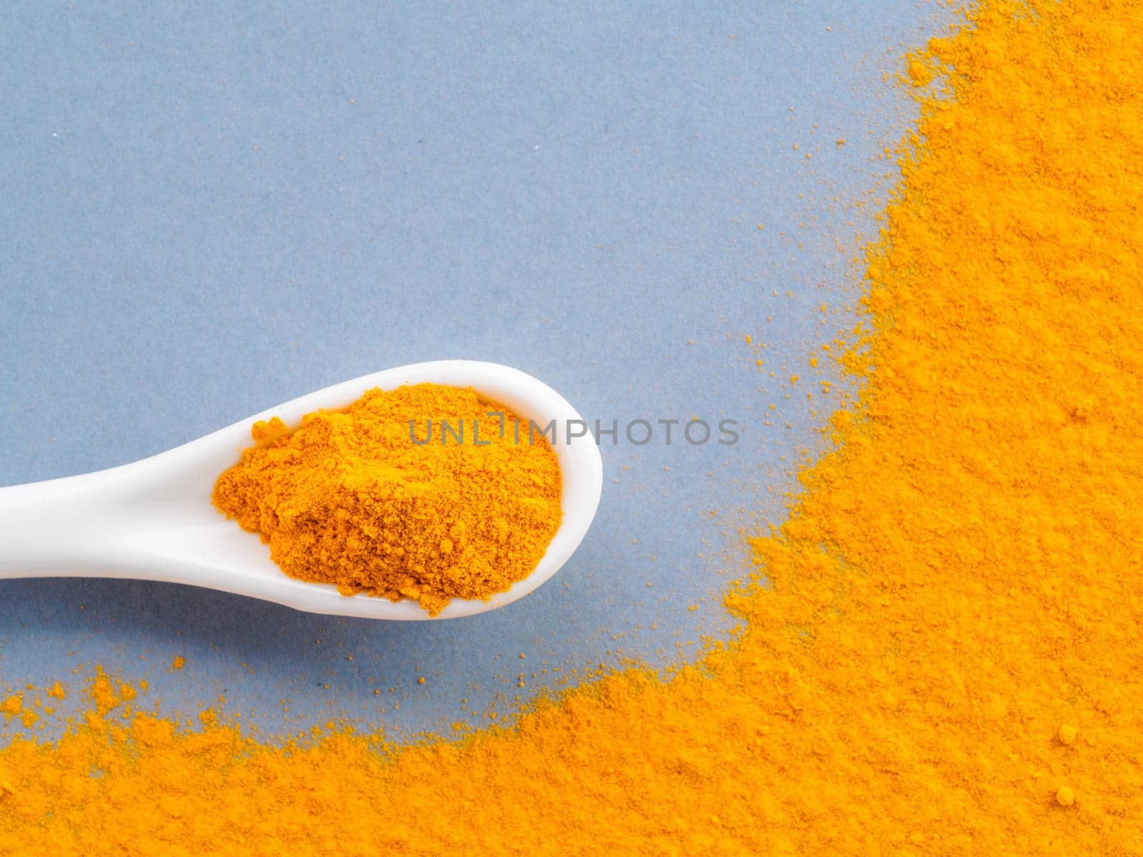 Turmeric Powder or Curcuma longa and white spoon with turmeric powder on gray background. Top view. Copy space for text.