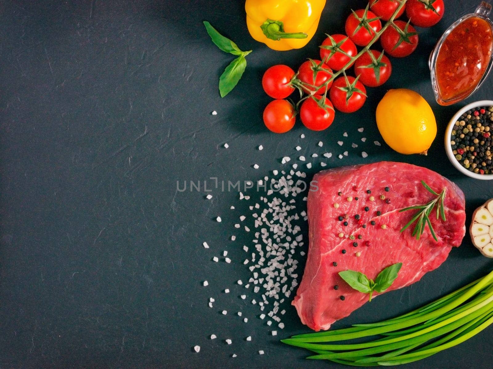 Raw meat. Raw beef steak on dark board with fresh herbs, vegetables, seasonings and spices. Top view or flat lay. Copy space