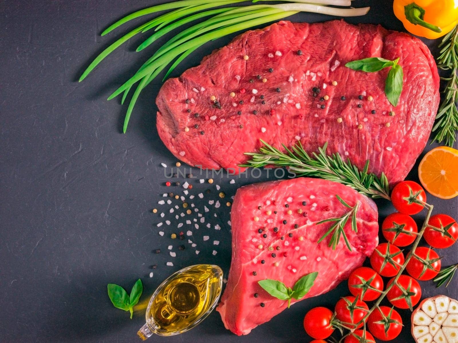 Raw meat. Raw beef steak on dark board with fresh herbs, vegetables, seasonings and spices. Top view or flat lay. Copy space