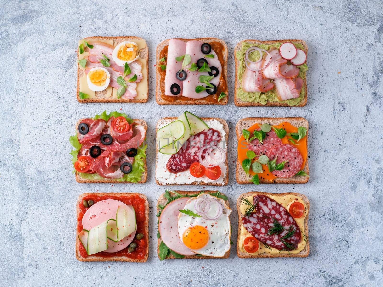 Set of eight different sandwiches with meat in square shape. Top view or flat lay. Assortment meat toasts on gray cement background. Idea, creative concept for sausage maker