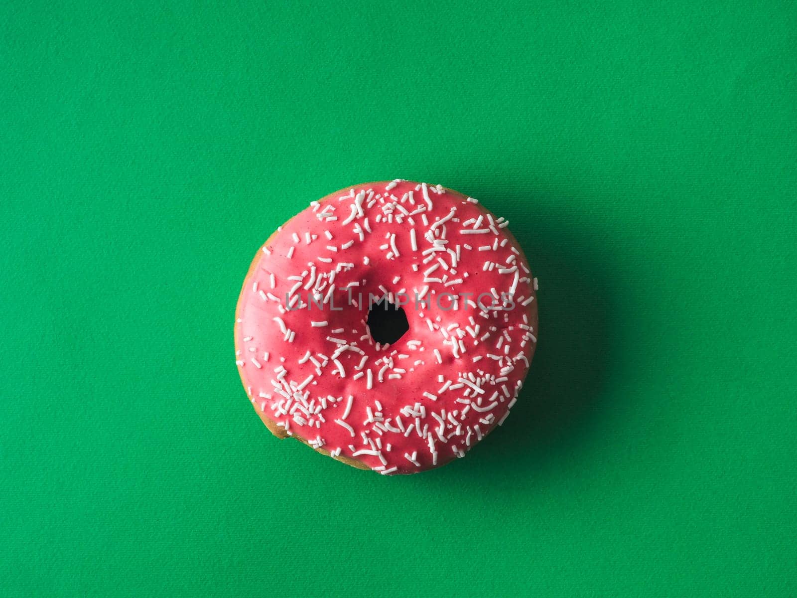 Top view of pink glazed donut on green background. Glazed and topping sprinkle pink doughnut on rich green background. Top view or flat lay.