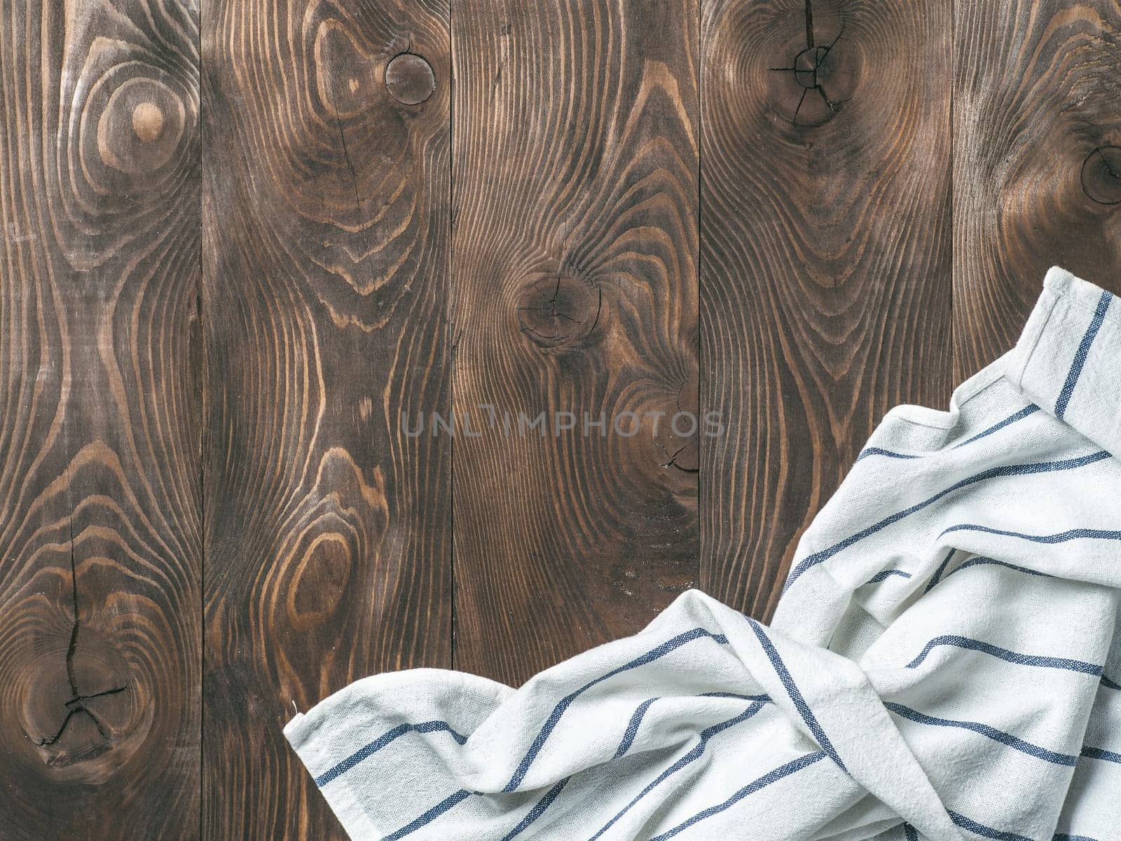 View from above on brown wooden table with linen kitchen towel or textile napkin. Blue tablecloth on dark brown wood tabletop. Copy space for text. Can use as mock up for design