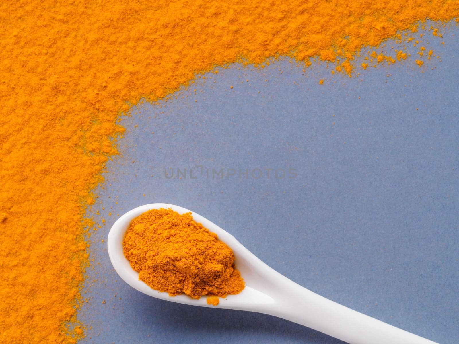 Turmeric Powder or Curcuma longa and white spoon with turmeric powder on gray background. Top view. Copy space for text.