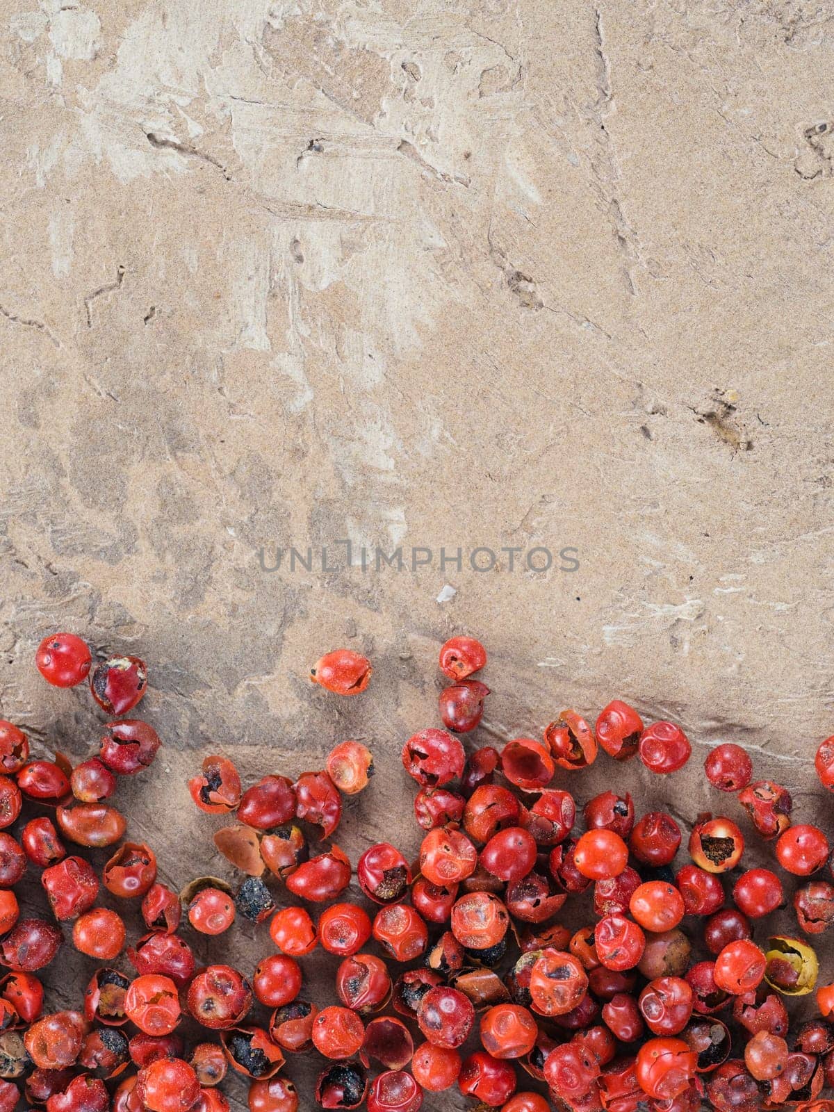 Background with dried pink pepper berries on brown concrete background. Top view of pink peppercorn. Copy space.