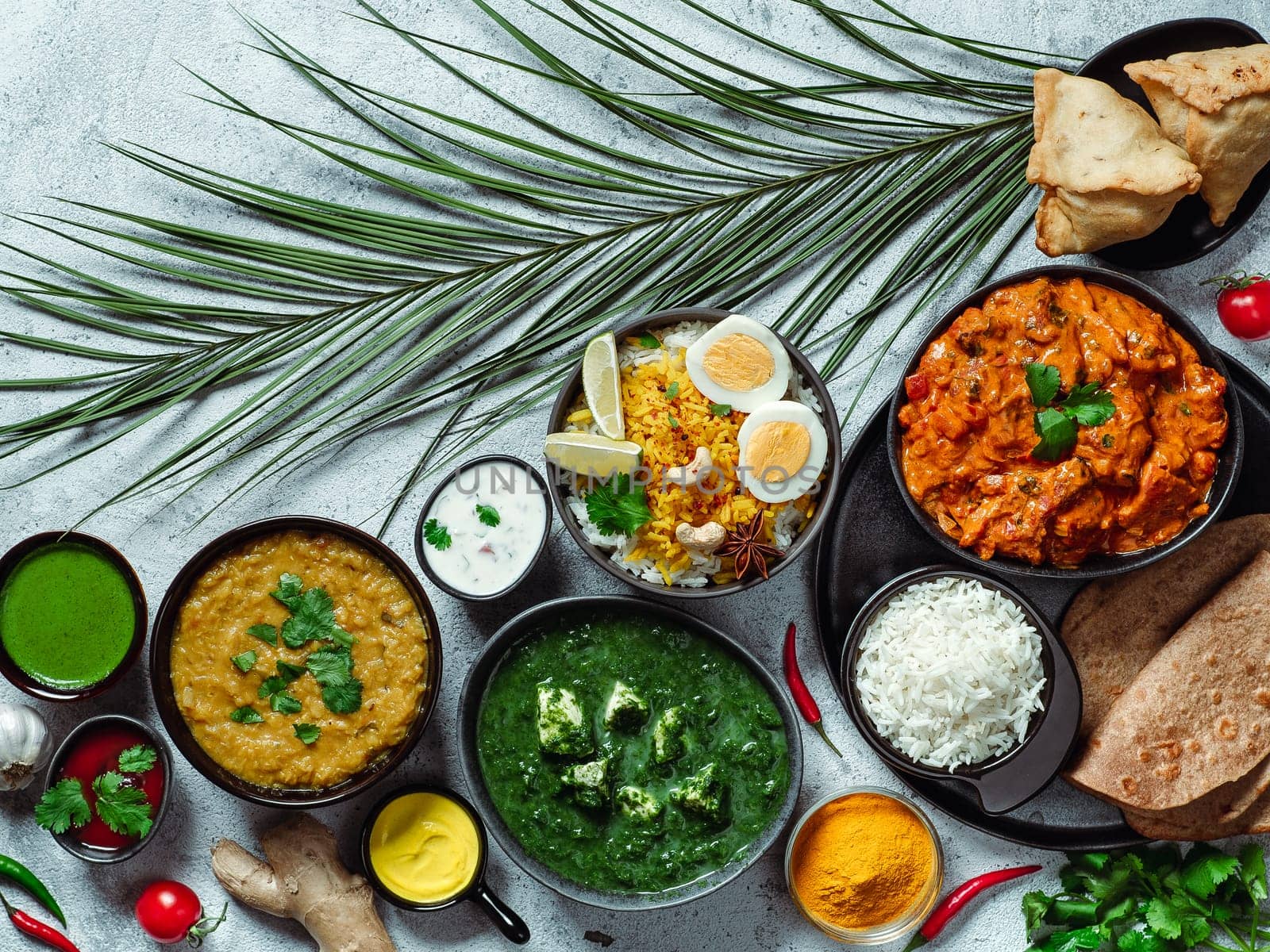 Indian cuisine dishes: tikka masala, dal, paneer, samosa, chapati, chutney, spices. Indian food on gray background. Assortment indian meal top view or flat lay. Copy space for text.