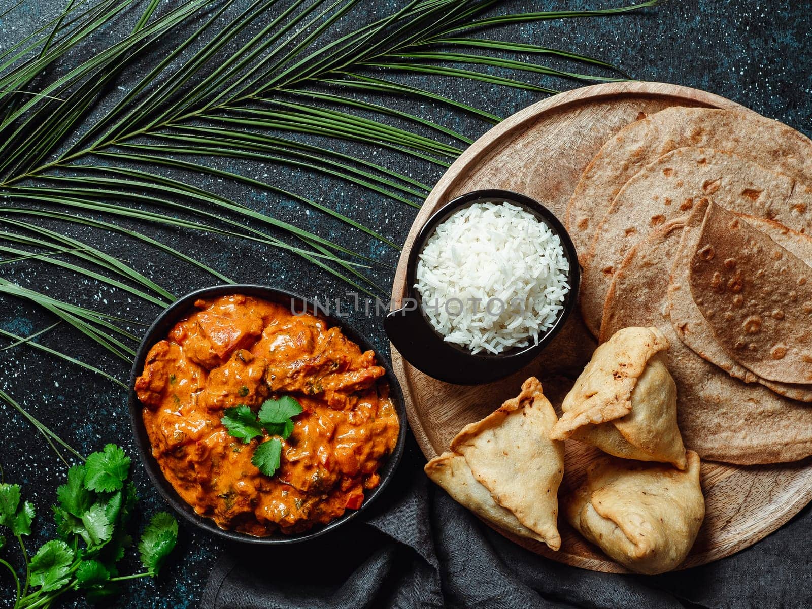 Indian cuisine dishes: tikka masala, rice, samosa, chapati,. Indian food on dark background with copy space. Assortment indian meal top view or flat lay.