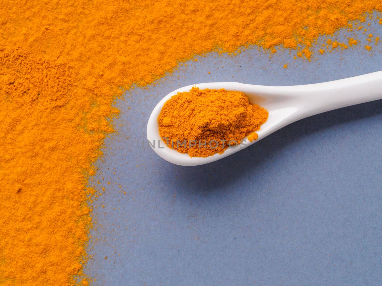 Turmeric Powder or Curcuma longa and white spoon with turmeric powder on gray background. Top view. Copy space for text.