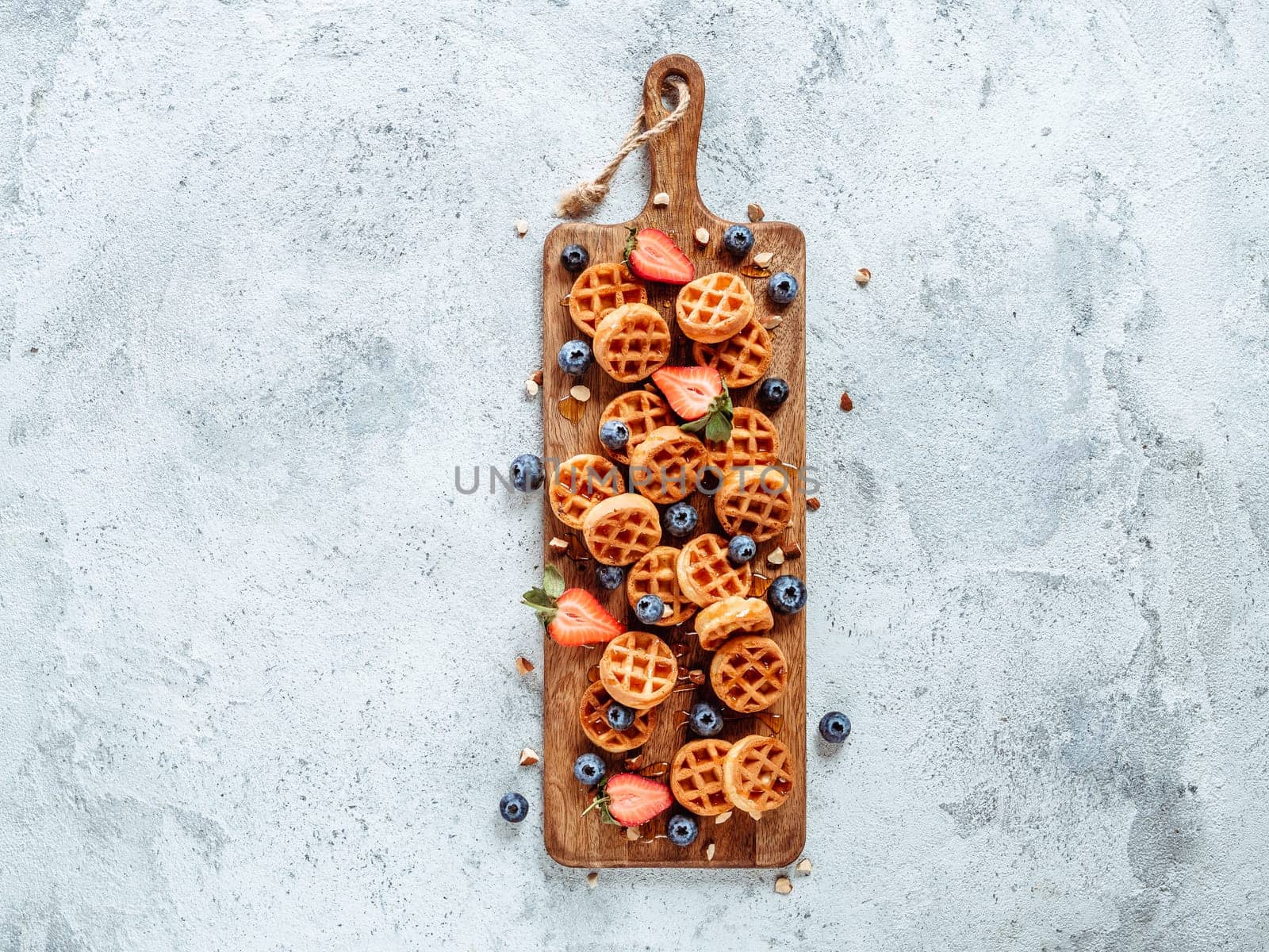 Small round delicious soft belgian waffles on cutting board. Fresh belgian waffles with berries and caramel sauce top view. Copy space for text or mock up