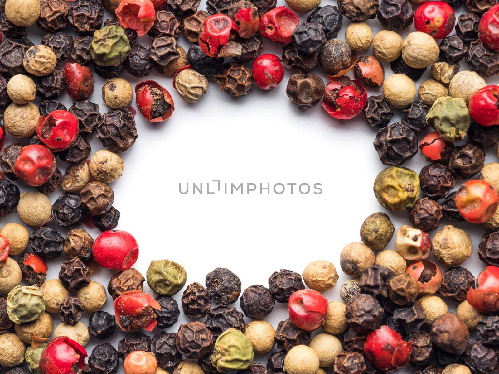 Mixed peppercorns background with white copy space in center. Food background with peppercorns. Different colored peppercorns pattern on white background, top view or flat lay