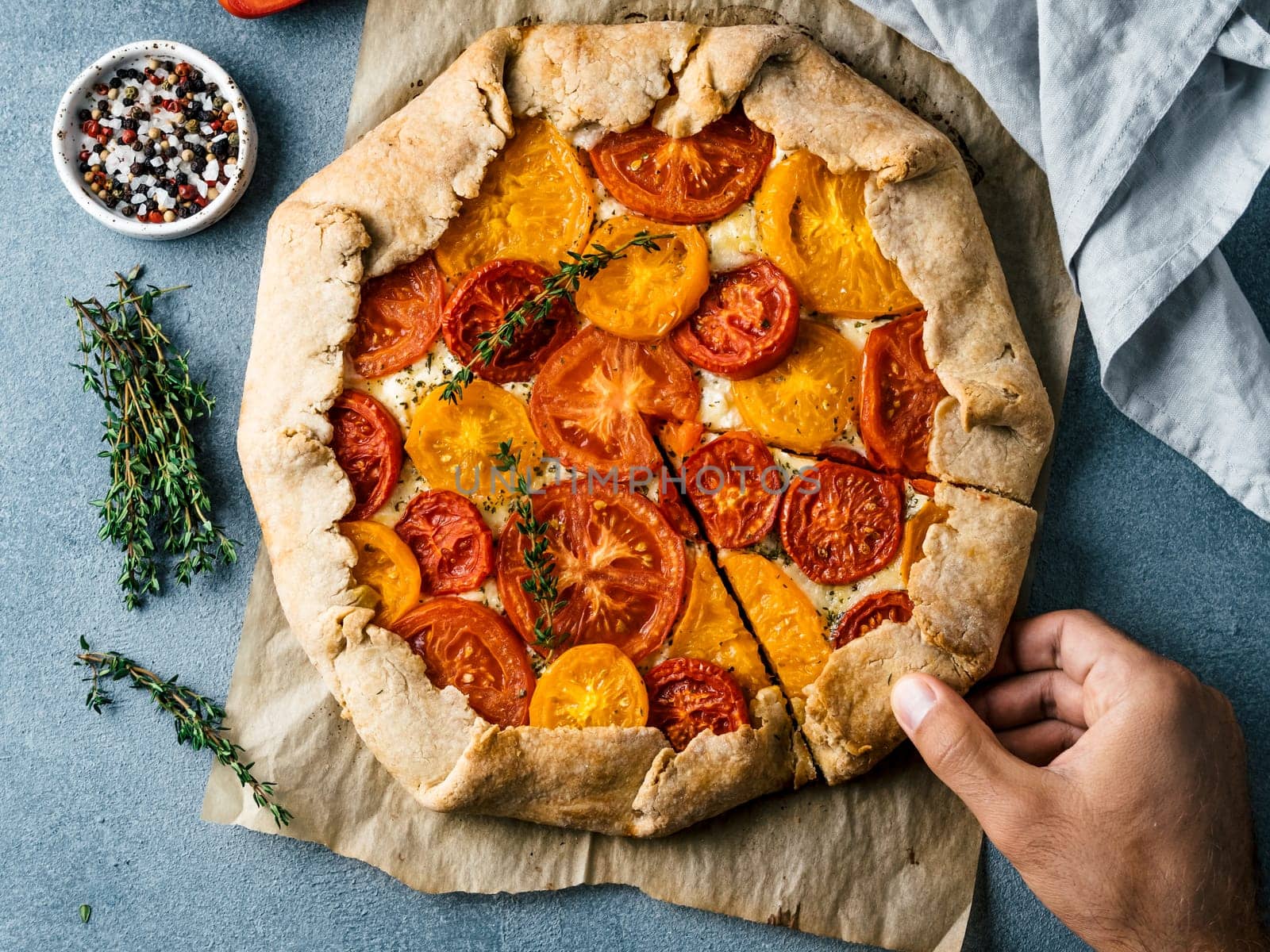 Savory fresh homemade tomato tart or galette.Hand takes piece of pie.Ideas and recipes healthy lunch,appetiezer-whole wheat or rye-wheat pie with tomatoes and cheese.Harvest tomatoes.Top view
