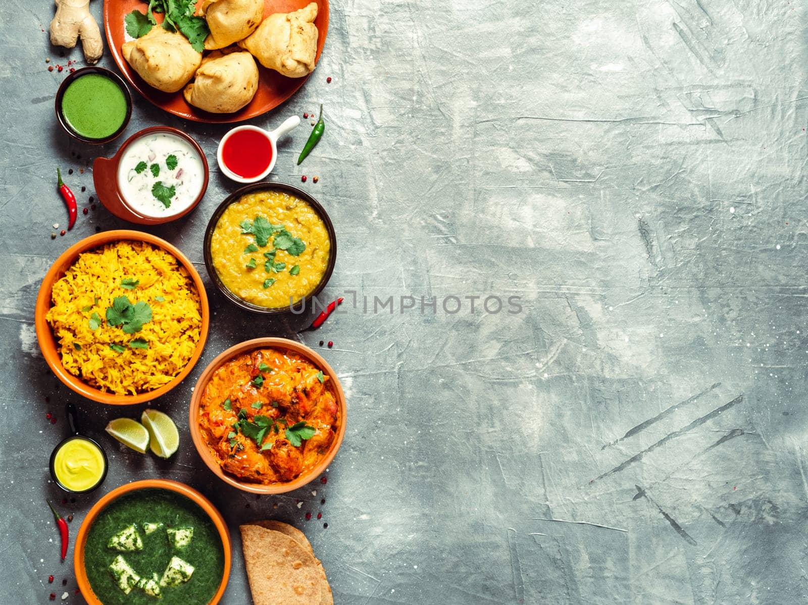Indian cuisine dishes: tikka masala, dal, paneer, samosa, chapati, chutney, spices. Indian food on gray background. Assortment indian meal with copy space for text. Top view or flat lay.