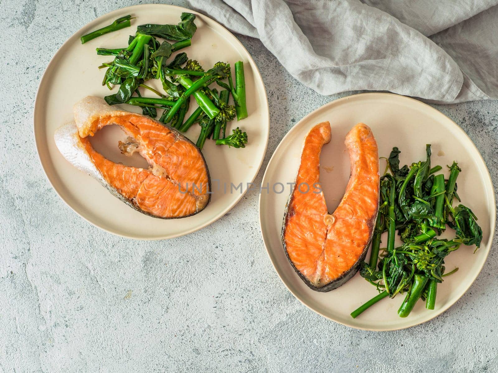 Ready-to-eat grilled salmon steak and greens - baby broccoli or broccolini and spinach on rustic craft plate over gray background. Keto diet dish. Top view or flat lay. Copy space for text or design.