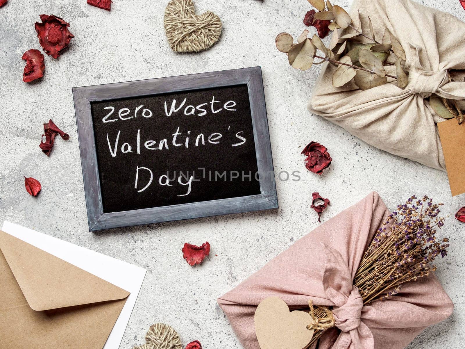 Zero waste Valentine's Day concept. Eco-friendly gift cloth wrapping in Furoshiki style and chalkboard with Zero Waste Valentine's Day letters on gray textured background. Top view or flat lay