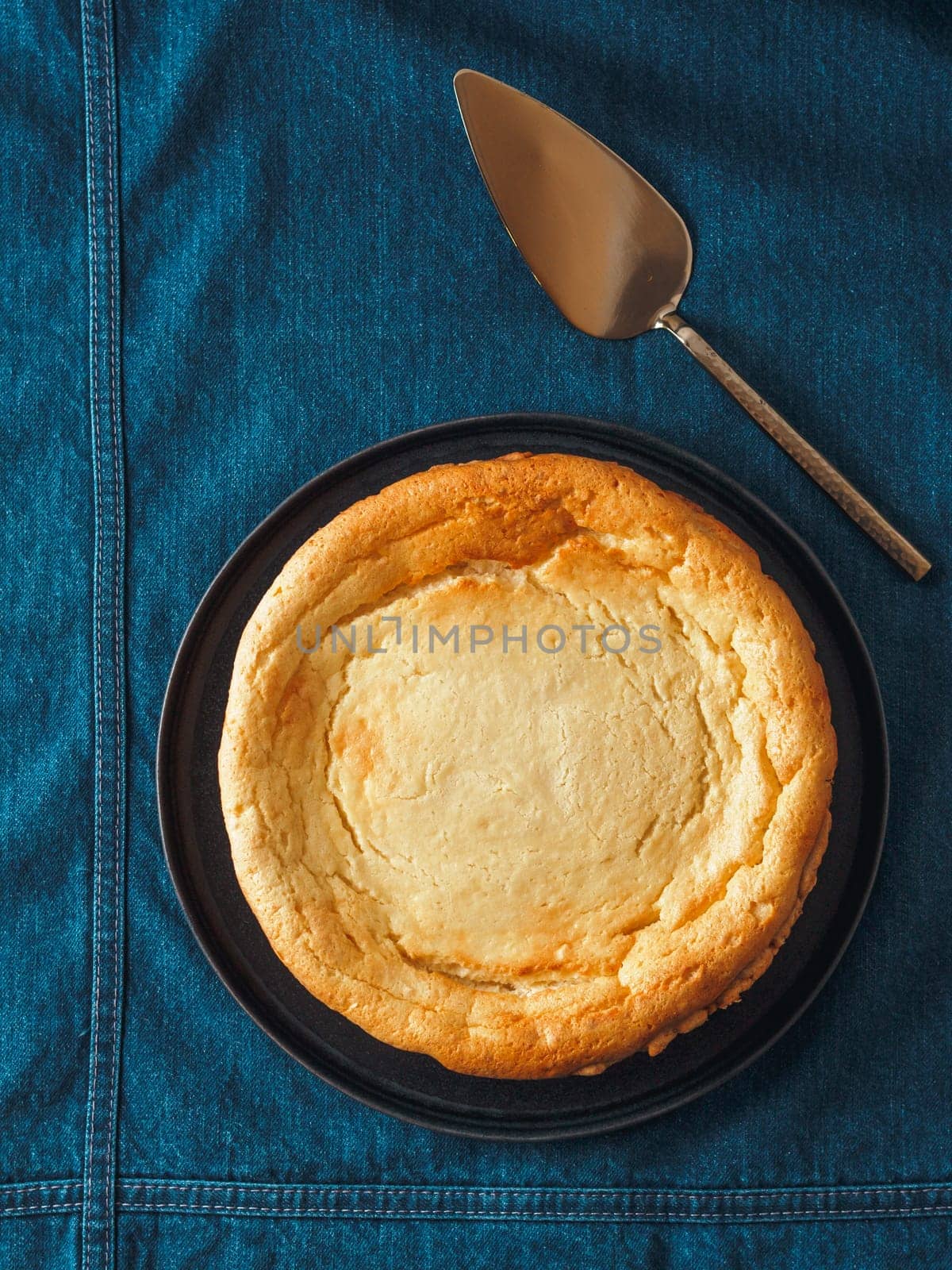 Plate with whole cheesecake pie on table with jeans tablecloth. Classic cheesecake flat lay or top view. Vertical.