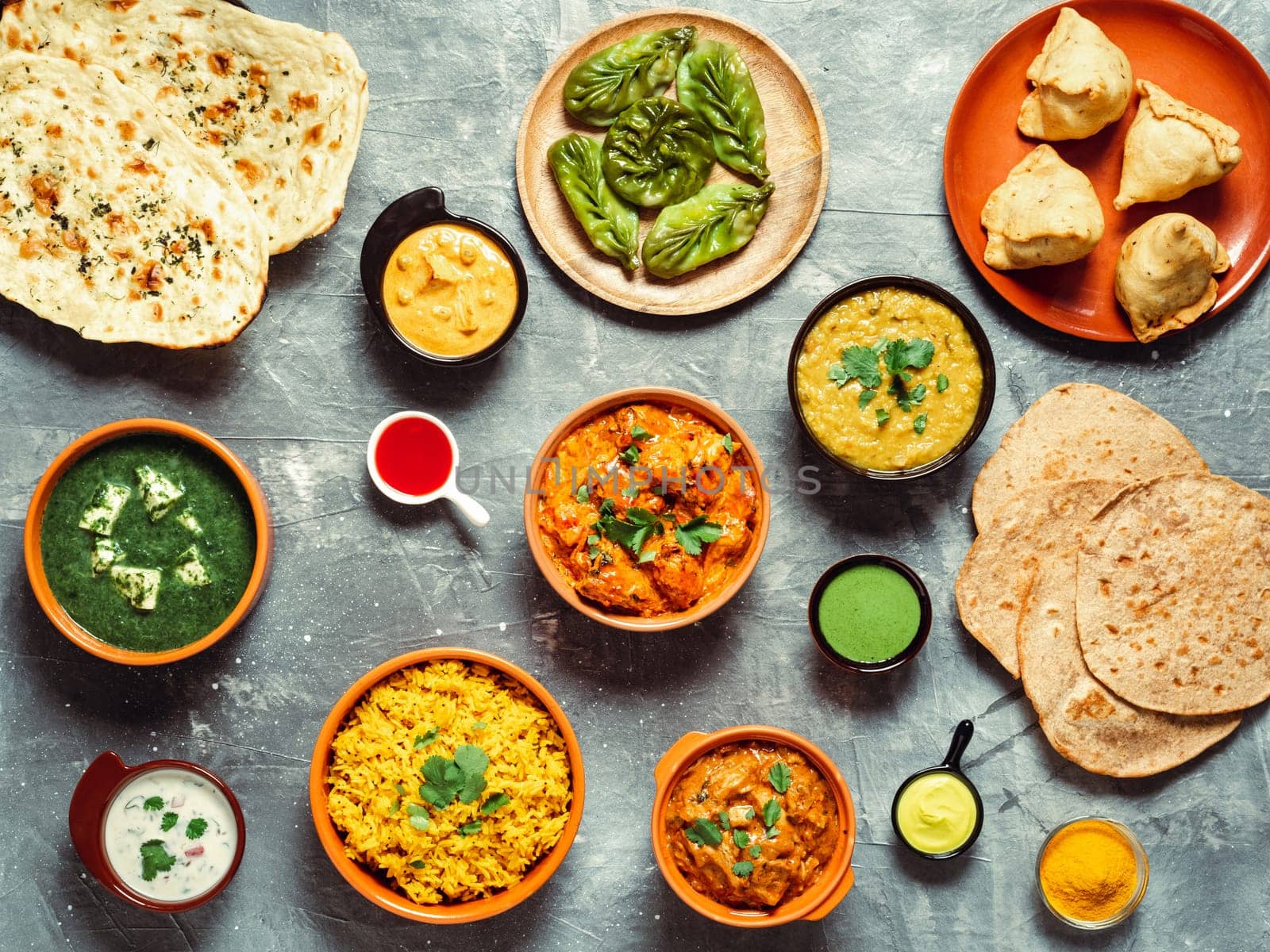 Indian cuisine dishes: tikka masala, dal, paneer, samosa, chapati, chutney, spices. Indian food on gray background. Assortment indian meal top view or flat lay.