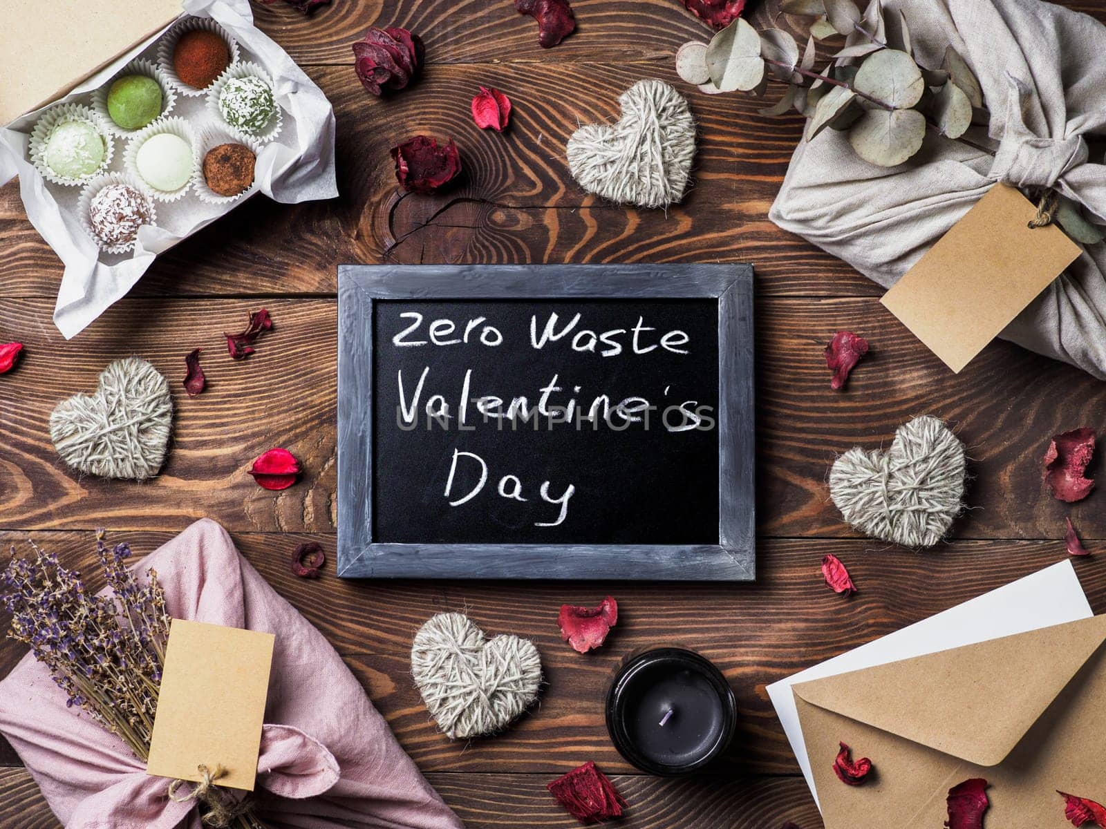 Zero waste Valentine's Day concept. Eco-friendly gift cloth wrapping in Furoshiki style, homemade sweets as gift ideas and chalkboard with Zero Waste Valentine's Day letters on brown wooden background