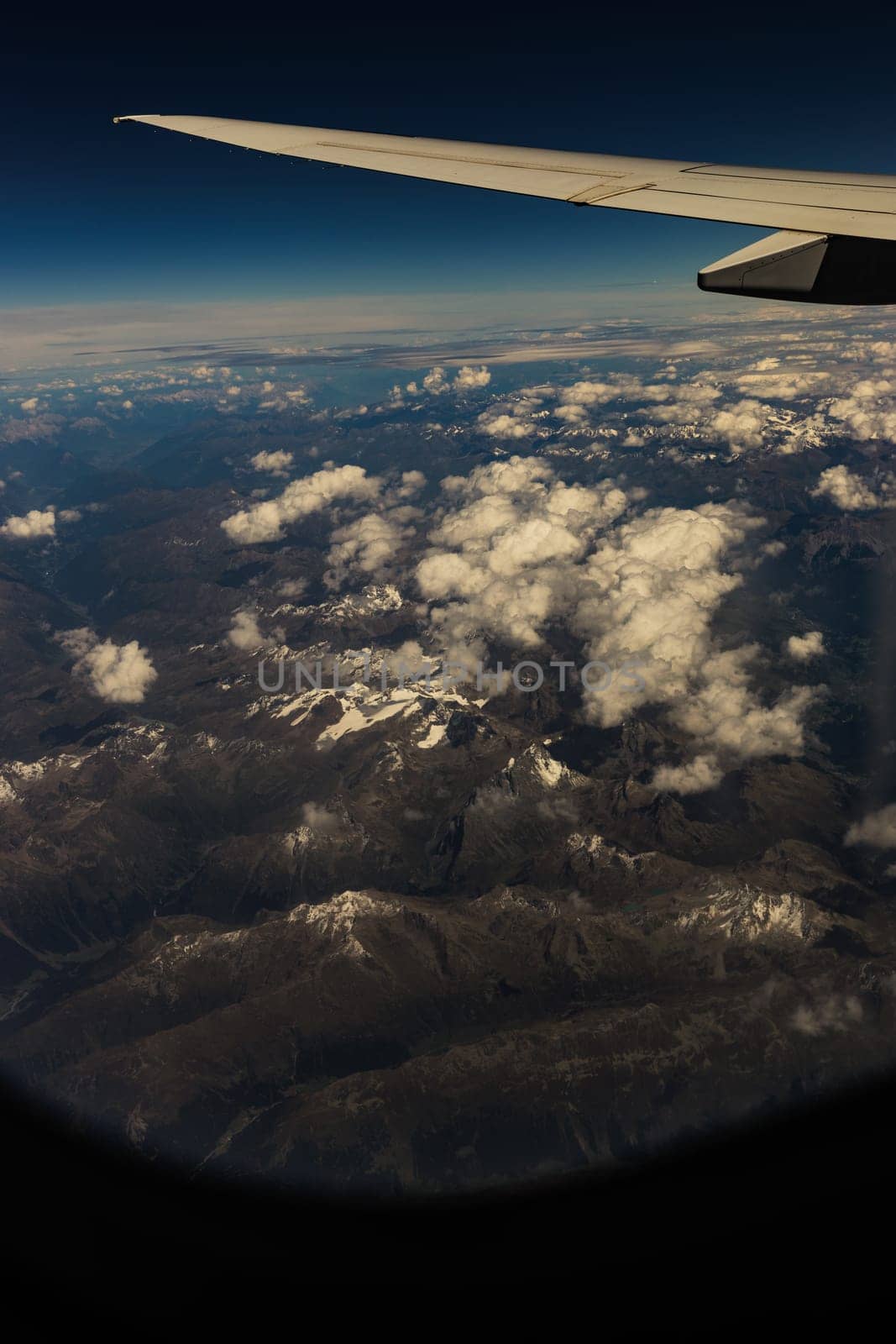 A beautiful view of an airplane wing, with rocky mountain tops in white clouds through the porthole window, close-up side view.