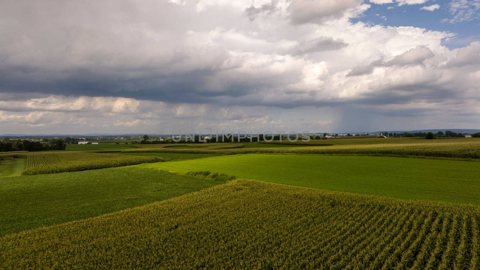 Dramatic storm clouds roll in over a patchwork of farmlands, highlighting the dynamic interplay between weather and agriculture.