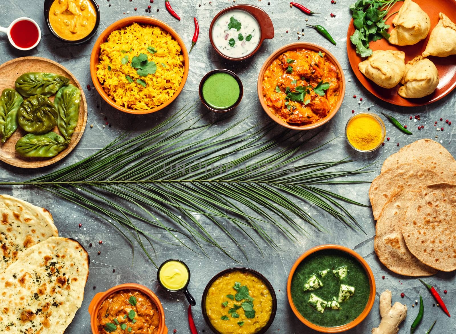 Indian cuisine dishes: tikka masala, dal, paneer, samosa, chapati, chutney, spices. Indian food on gray background. Assortment indian meal with copy space for text in center. Top view or flat lay.