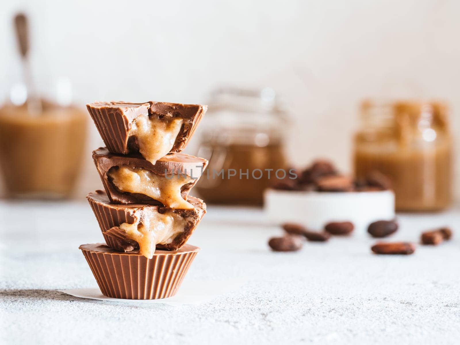 Stack of vegan chocolate cups with caramel on white tabletop. Homemade vegetarian chocolate caramel cups with raw cacao chocolate. Ideas and recipes for healthy sweets and dessert. Copy space for text
