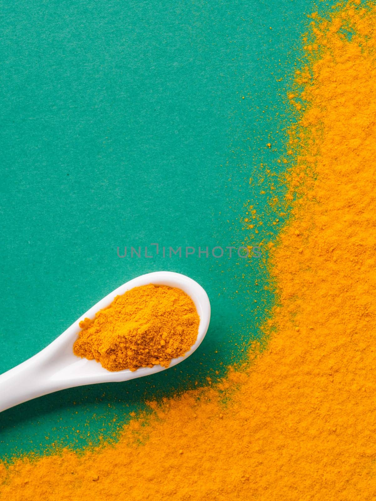 Turmeric Powder or Curcuma longa and white spoon with turmeric powder on green background. Top view. Copy space for text.