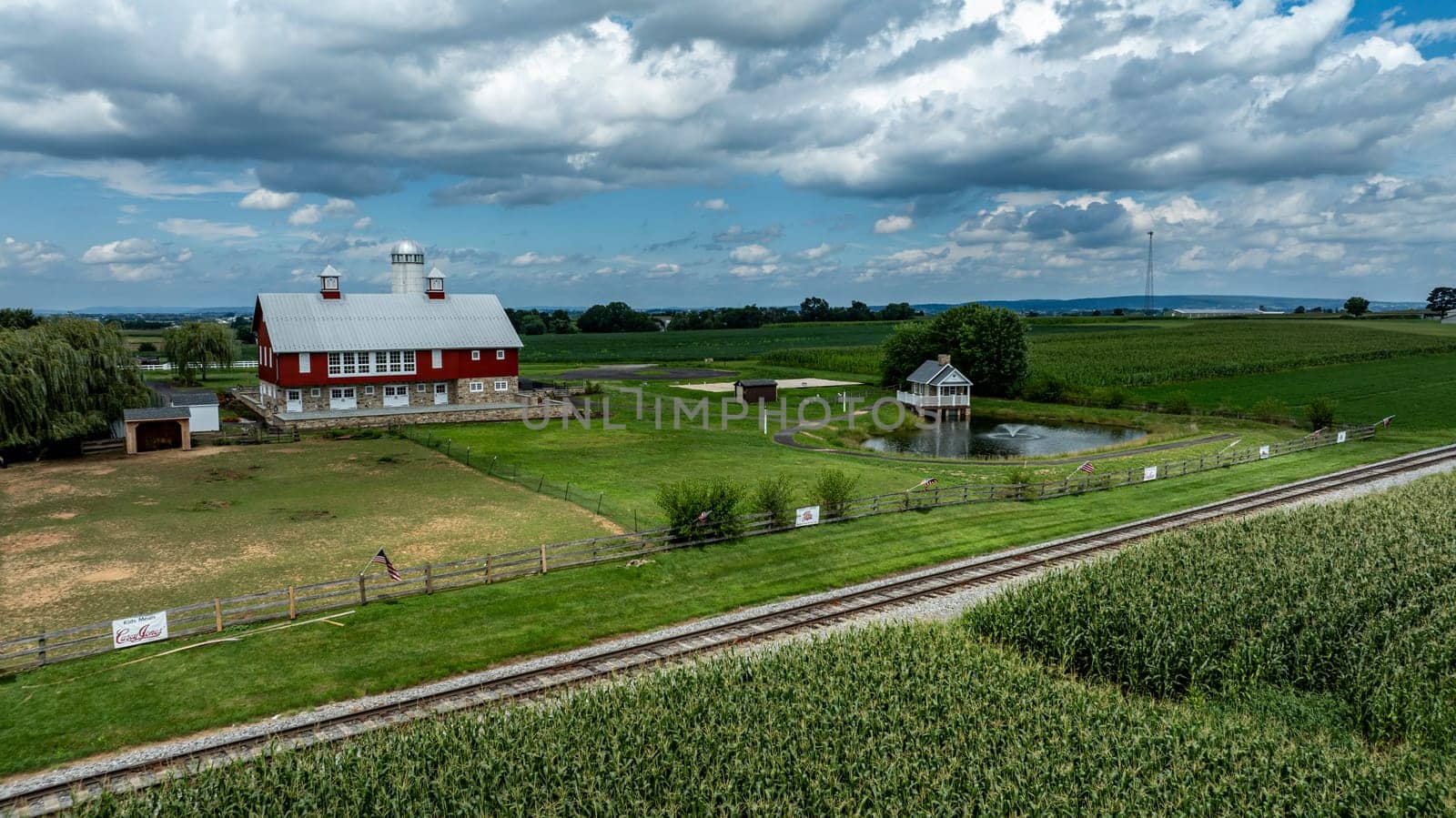 Ronks, Pennsylvania, August 15, 2023 - Dominating this pastoral scene is a classic red barn with a serene pond and gazebo, set against the rich tapestry of flourishing cornfields.