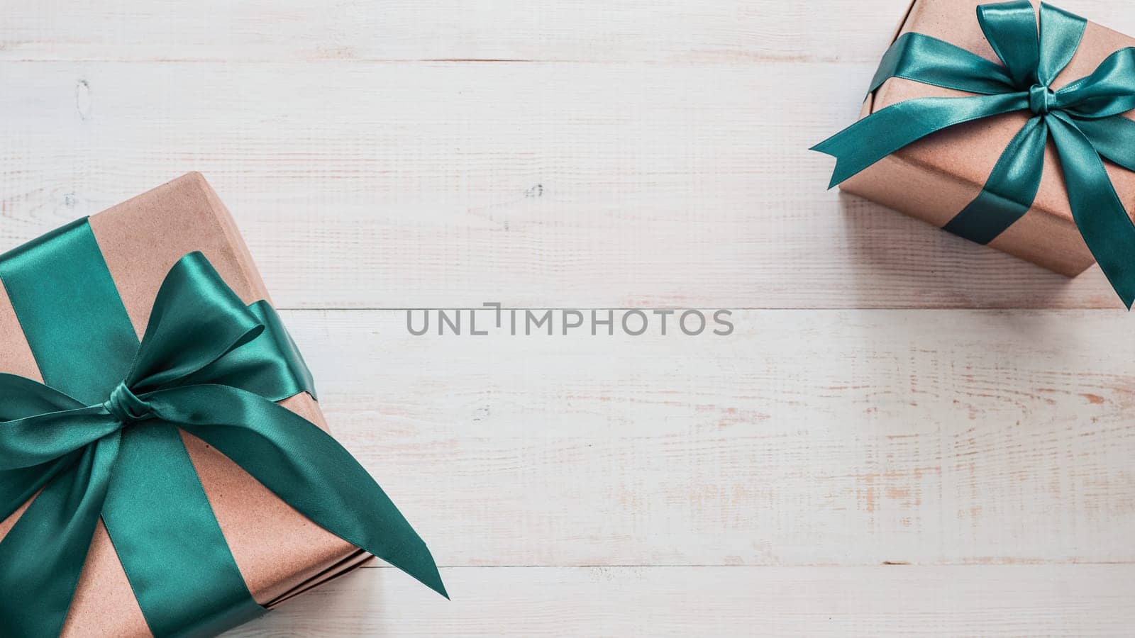 Two gift boxes in craft wrapping paper and green satin ribbon on white wooden table, copy space in center. Beautiful Christmas, New Year or Birthday presents, flat lay or top view. Banner