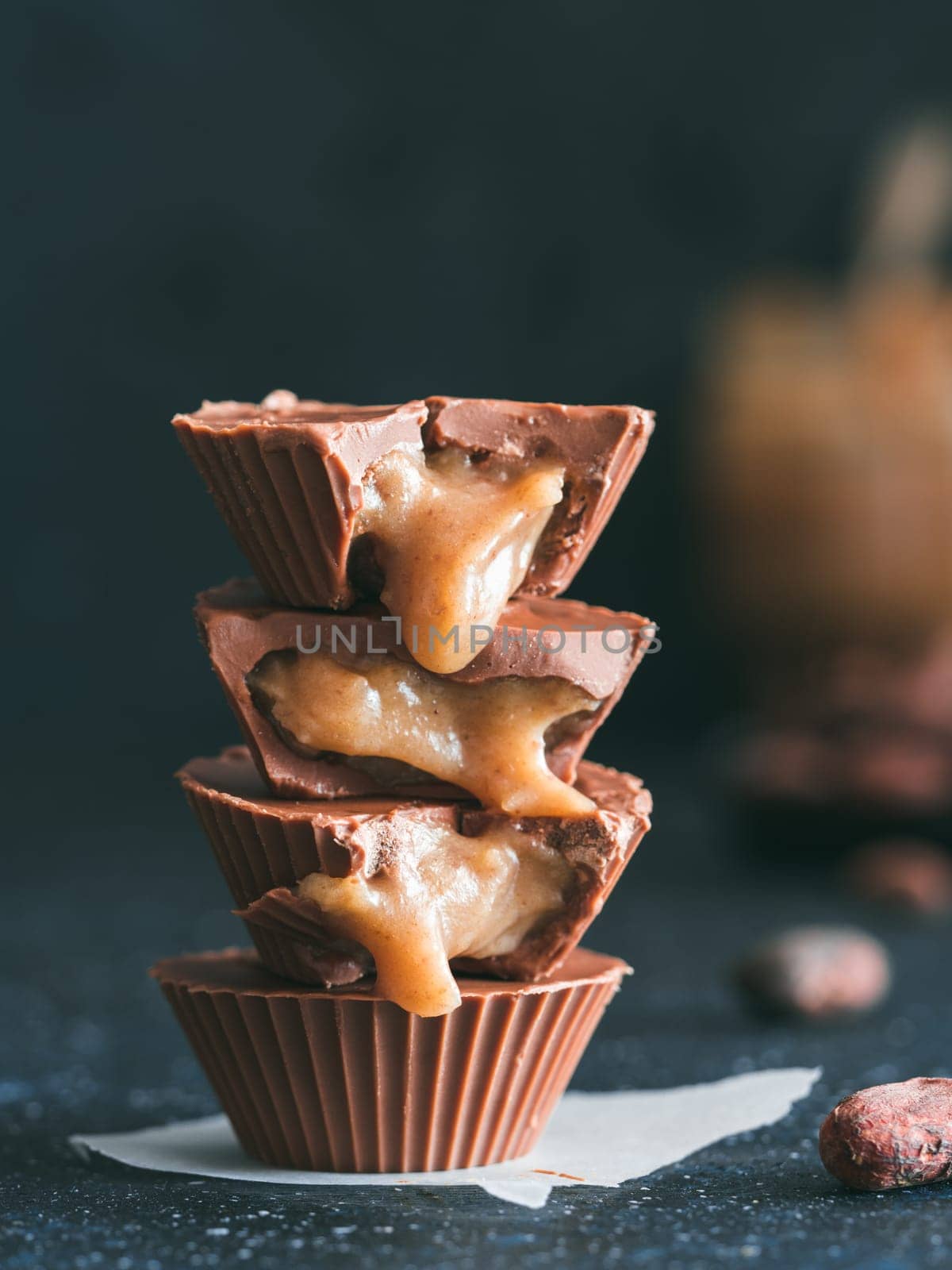 Stack of vegan chocolate cups with caramel on dark table. Homemade vegetarian chocolate caramel cups with raw cacao chocolate. Ideas and recipes for healthy sweet dessert. Copy space for text.Vertical