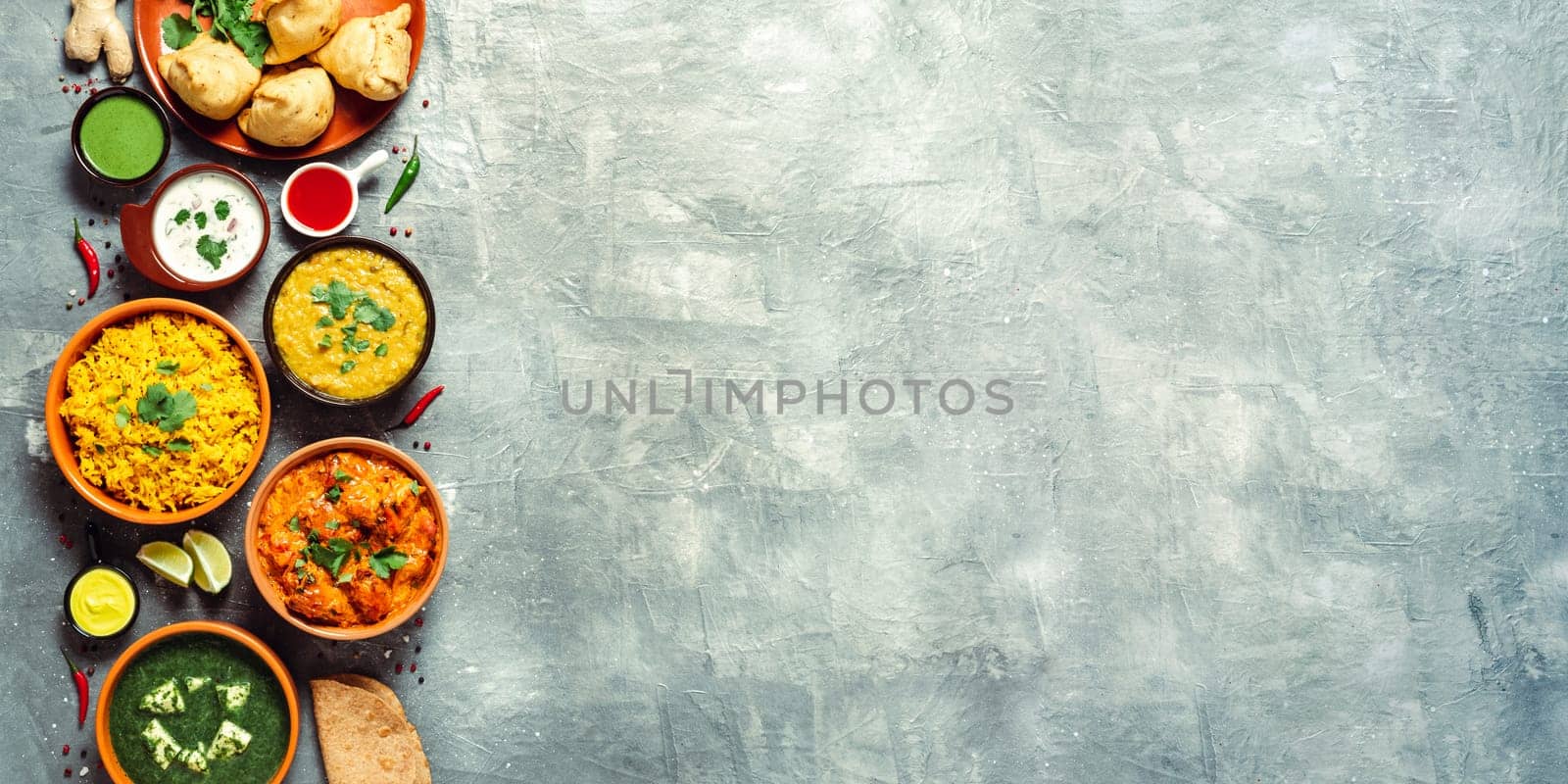 Indian cuisine dishes: tikka masala, dal, paneer, samosa, chapati, chutney, spices. Indian food on gray background. Assortment indian meal banner with copy space for text. Top view or flat lay.