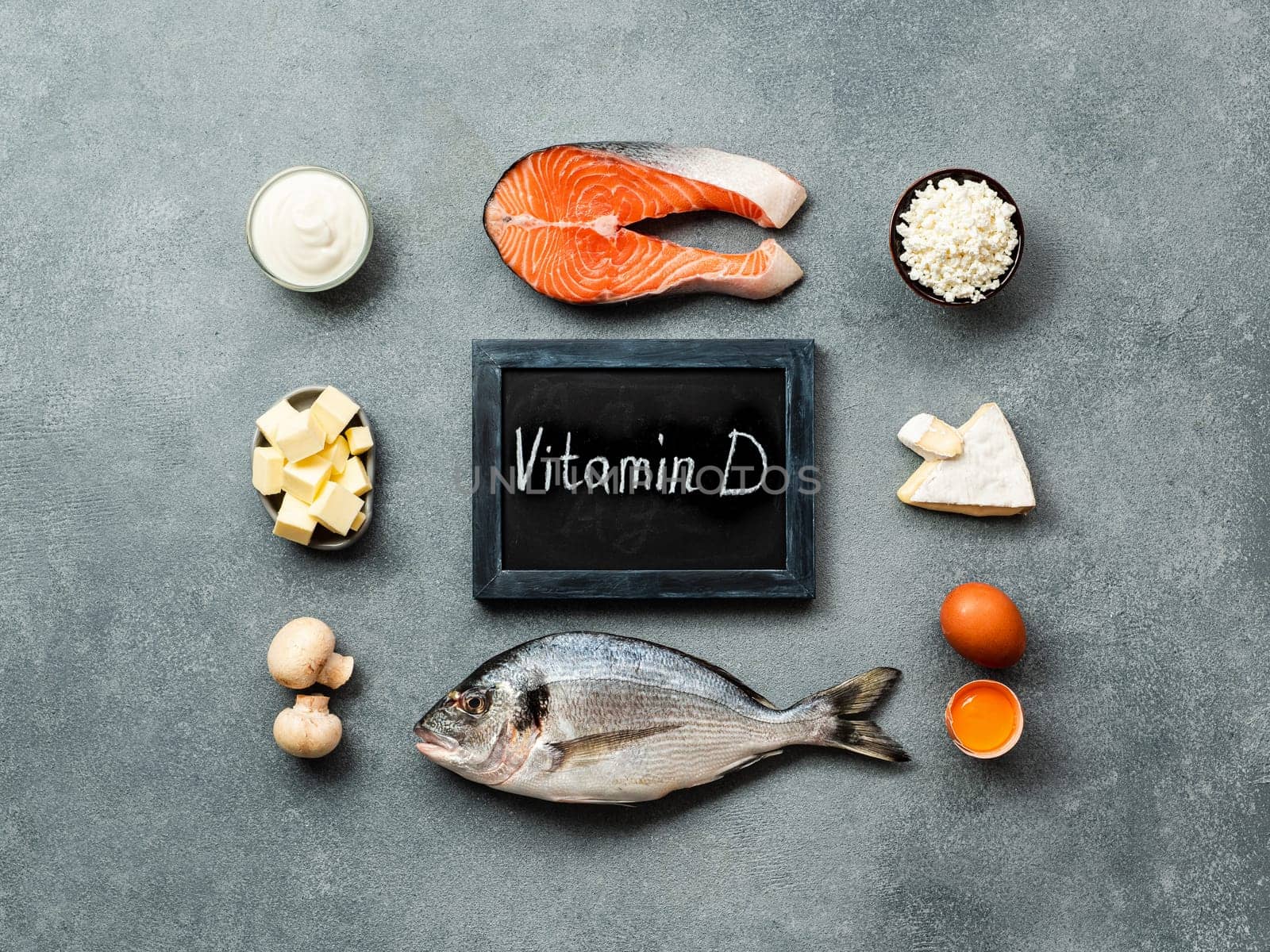 Vaitamin D sources concept. Fish, salmon, dairy products, eggs, mushrooms and chalkboard with Vitamin D words on gray stone background. Top view or flat lay.