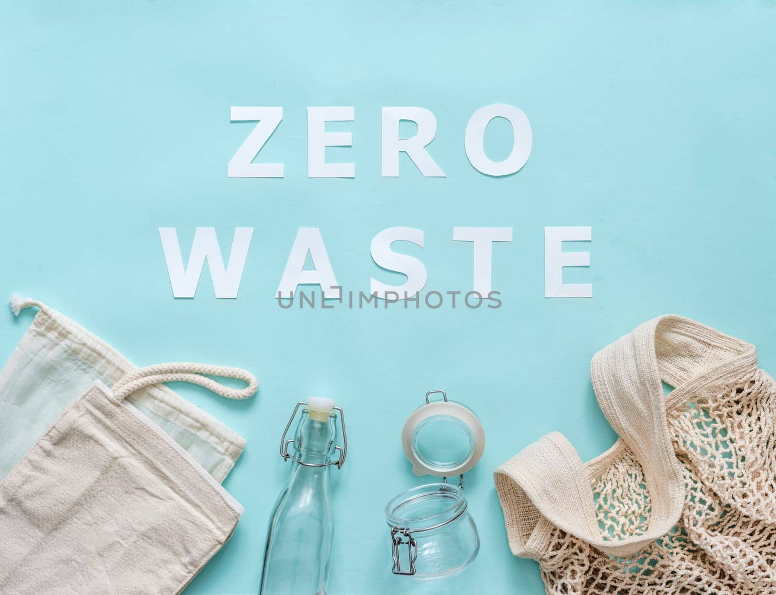 Zero waste concept. Textile eco bags, glass jar and bottle on blue background with Zero Waste white paper text. Eco friendly and reuse concept. Top view or flat lay
