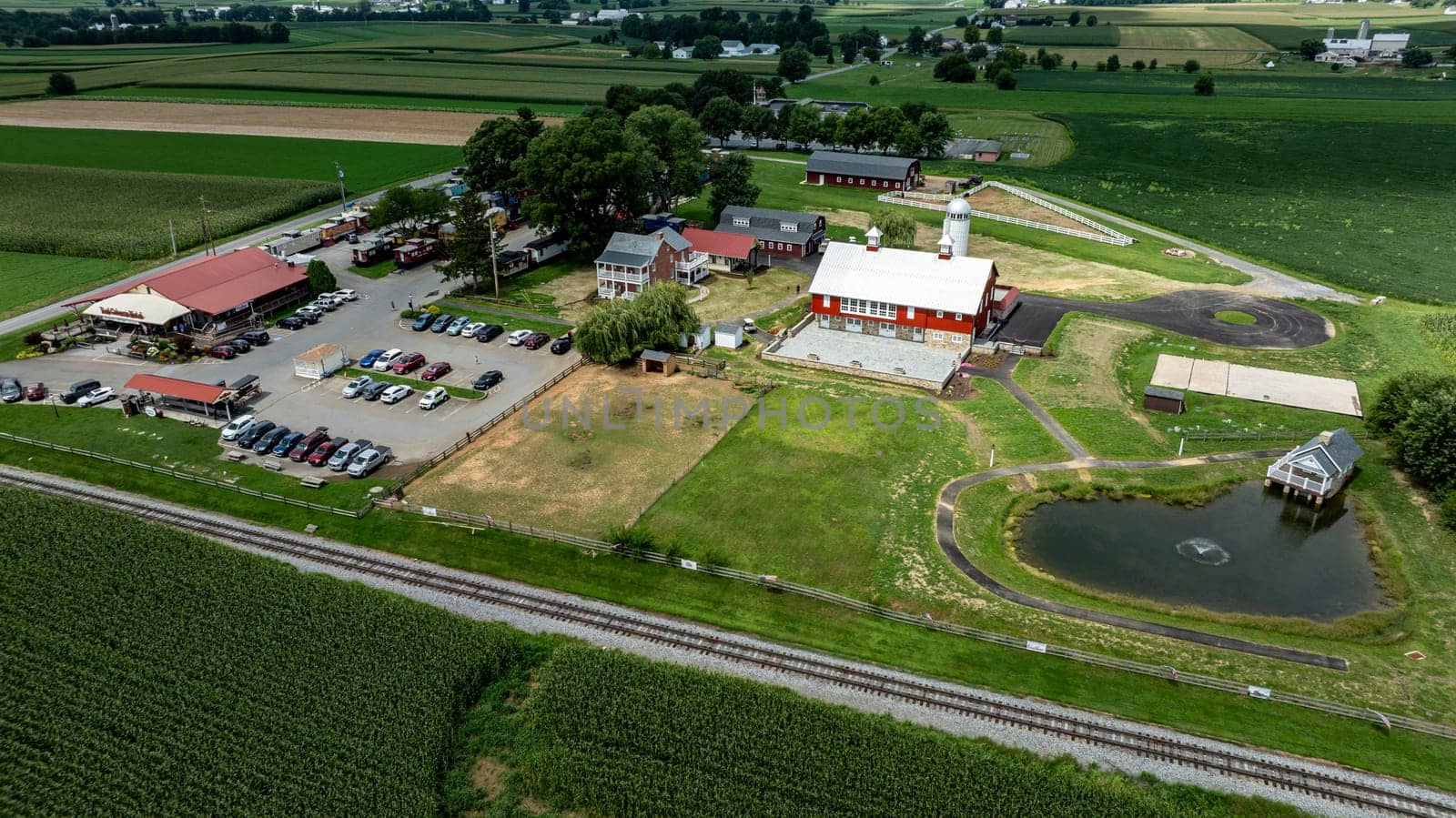 Ronks, Pennsylvania, August 15, 2023 - This vibrant aerial shot captures the active life of a rural complex, complete with a restaurant, parking, and a serene pond set against a backdrop of extensive farmland.