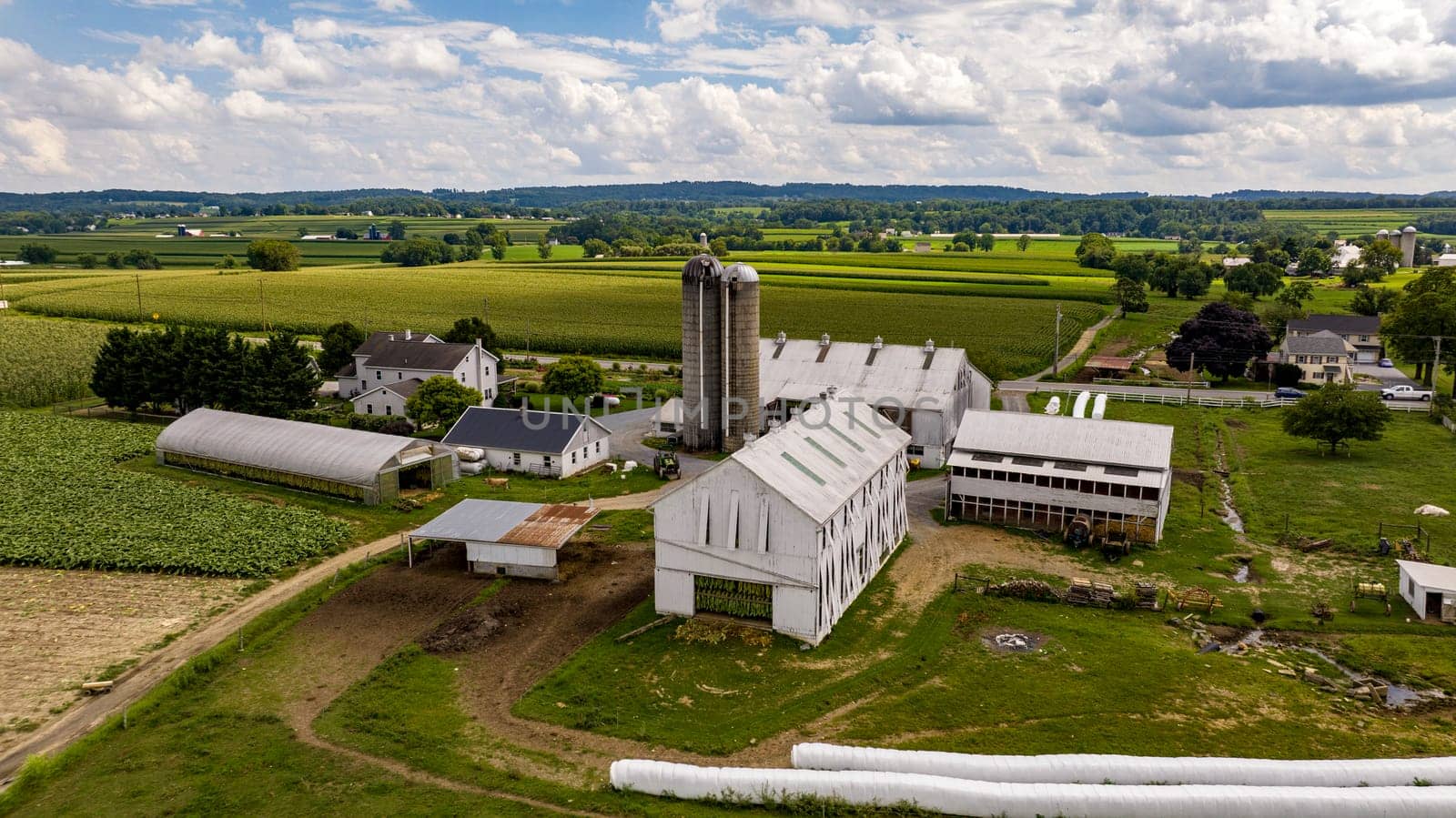 Ronks, Pennsylvania, August 15, 2023 - Above the patchwork fields, this traditional farm homestead stands with its silo and barns, a testament to timeless agricultural practices.