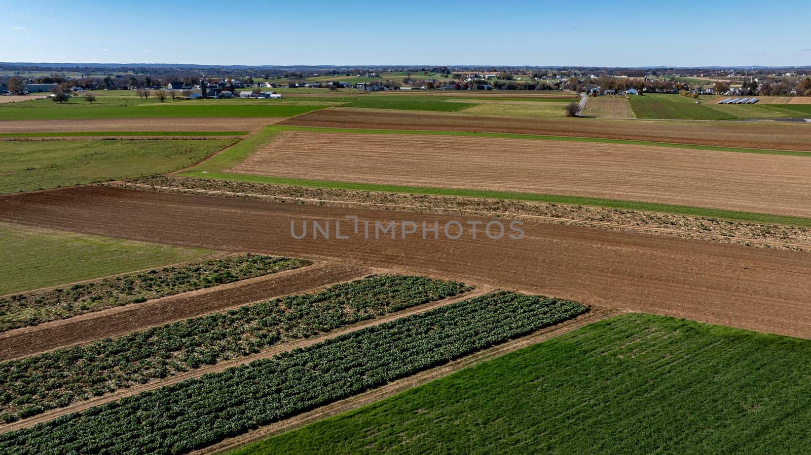 This high-angle shot captures a vast tapestry of farmland, with sections of rich soil ready for planting and others lush with crops. Ideal for agriculture and land management themes.