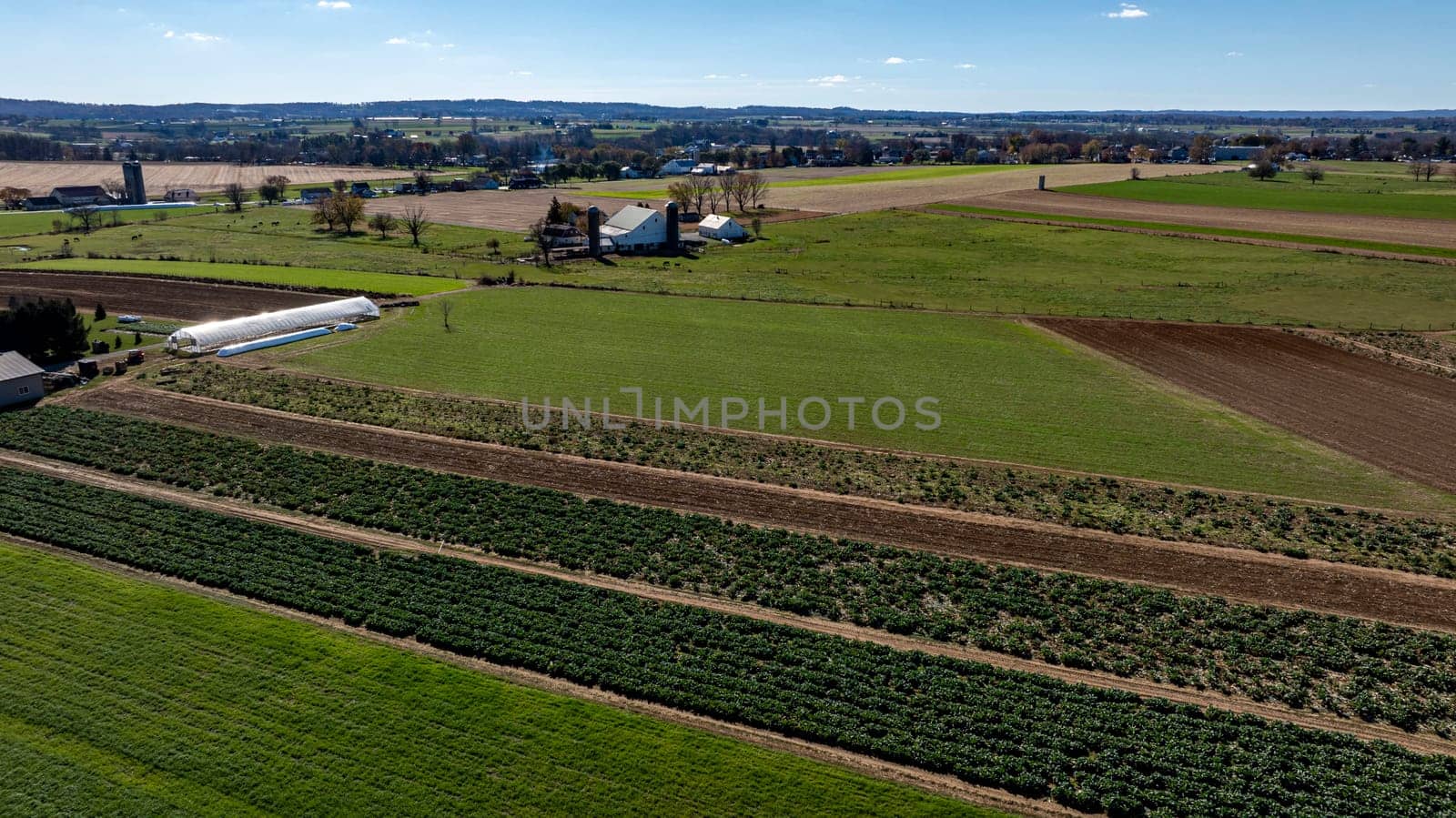 Aerial view of sprawling Lancaster, PA farms showing a quilted landscape of varying crops and a traditional farmstead bathed in sunlight.