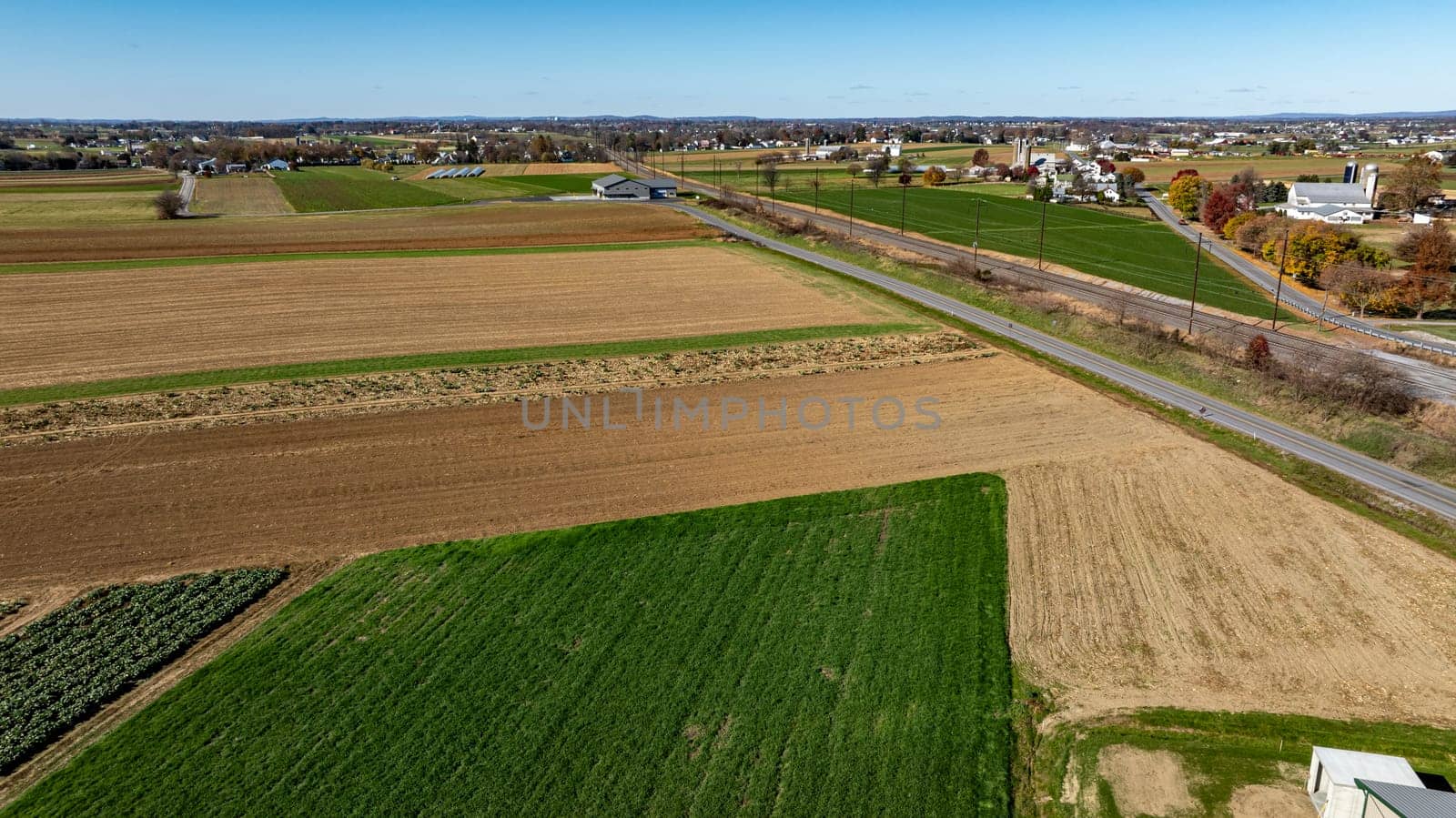 An expansive drone capture of farmland alongside a country road, showcasing a mix of fallow and verdant plots, suitable for discussions on rural development and land use.