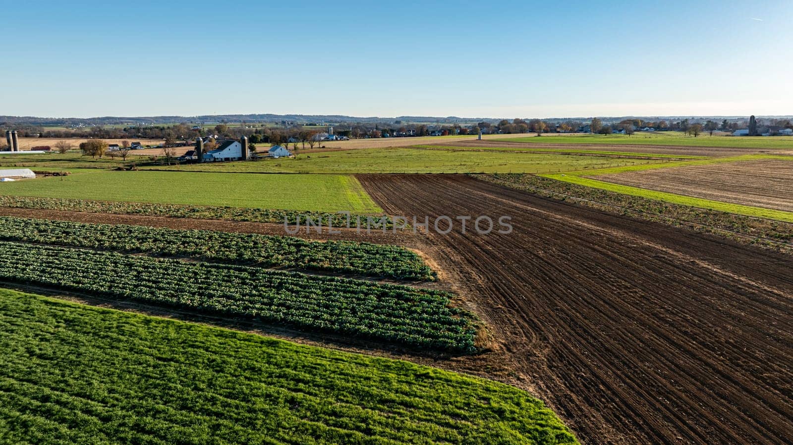 The image displays a bird's-eye view of diverse farm plots in the fall, creating a mosaic of harvest-ready fields and green spaces, perfect for agricultural themes.