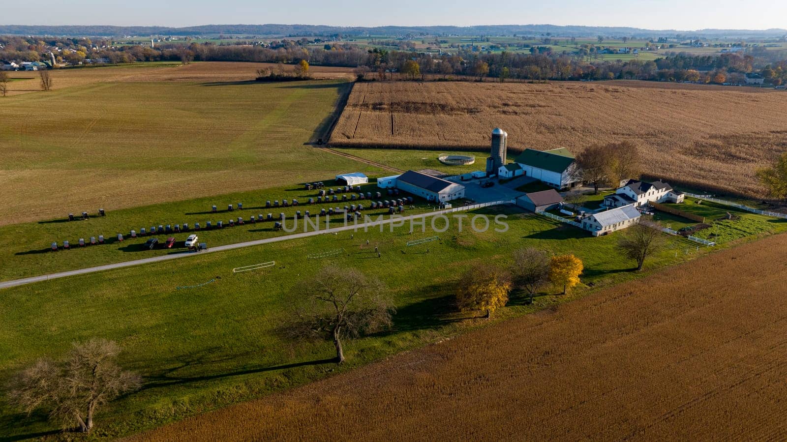 An aerial shot captures the sprawling expanse of a farm at dusk, with fields awaiting harvest and the rural landscape bathed in the soft light of the setting sun.