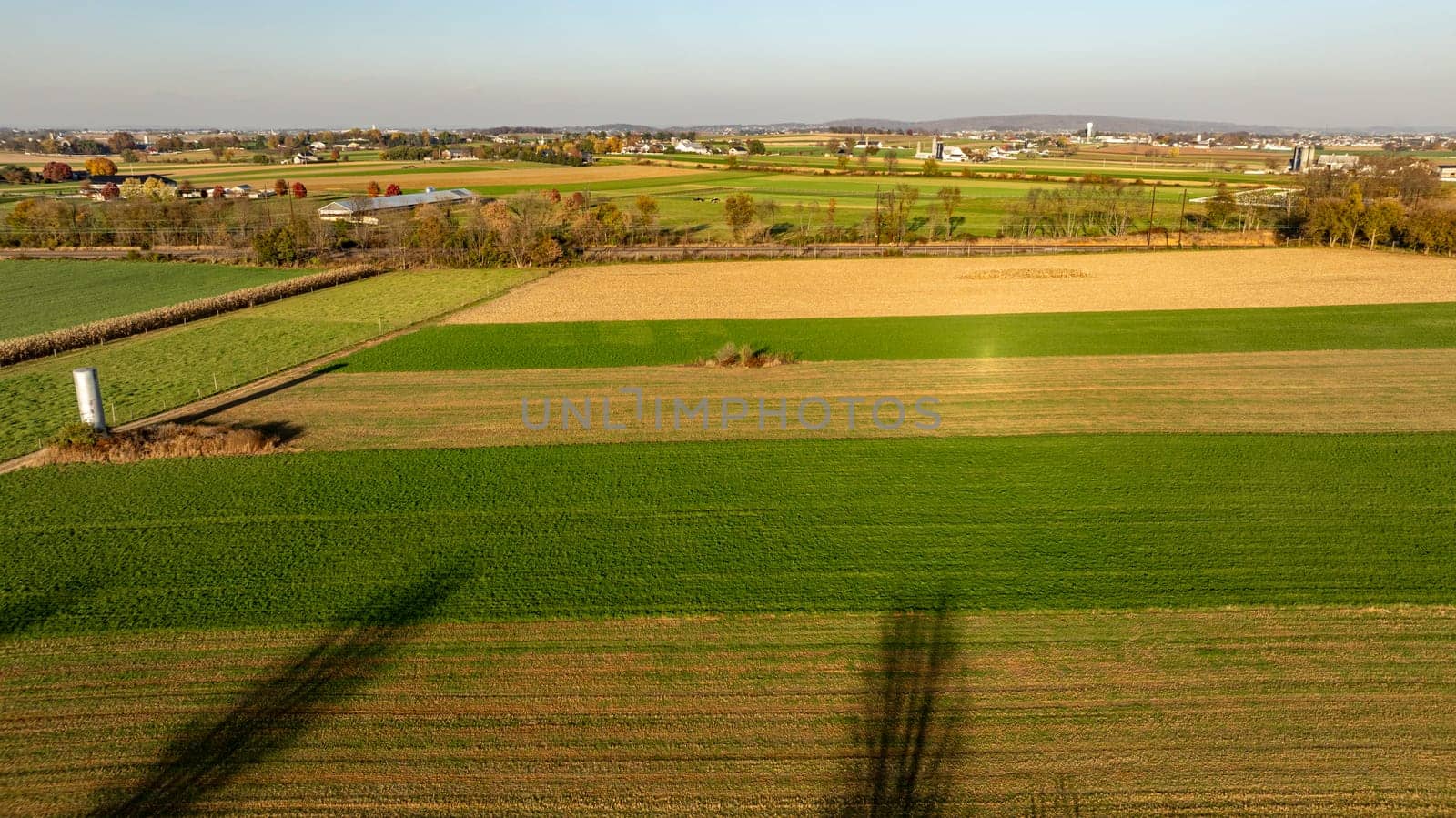 The warm light of the setting sun highlights a patchwork of agricultural fields, presenting a picturesque rural landscape from above.