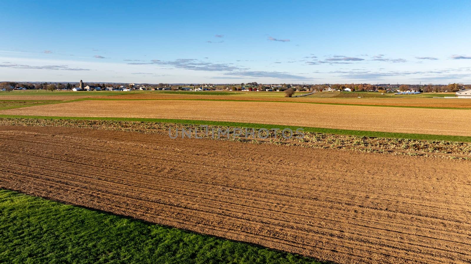 Late afternoon light bathes a patchwork of harvested and plowed fields in a rural landscape, symbolizing the end of a farming cycle.