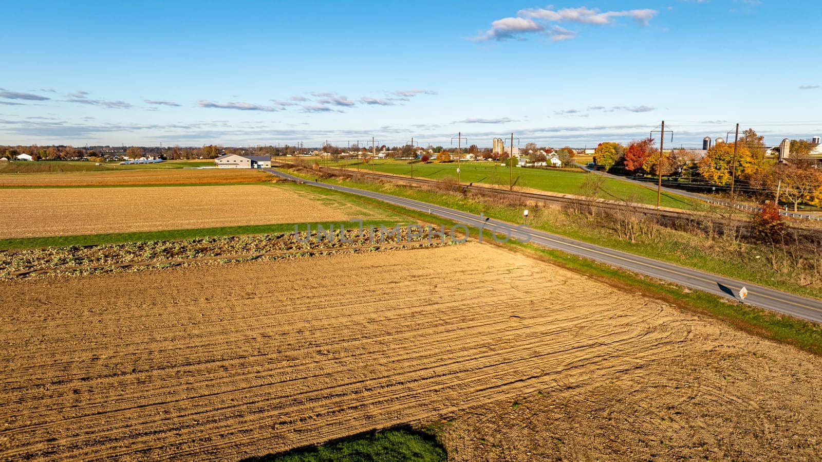 A serene aerial view captures the golden hour over diverse crop fields, with long shadows accentuating the rich textures of the farmland.