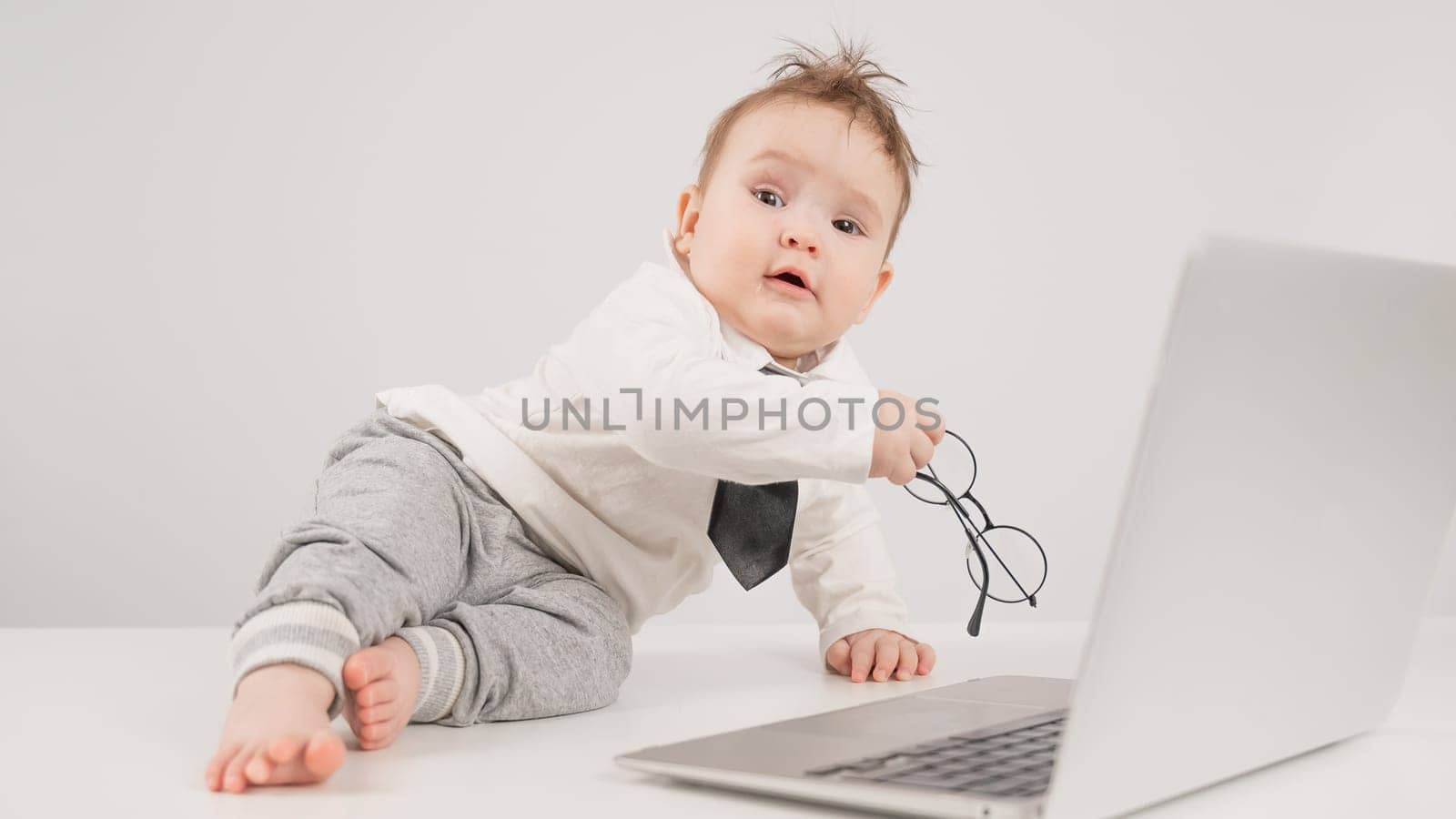 A cute child wearing a suit holds glasses and lies behind a laptop. by mrwed54
