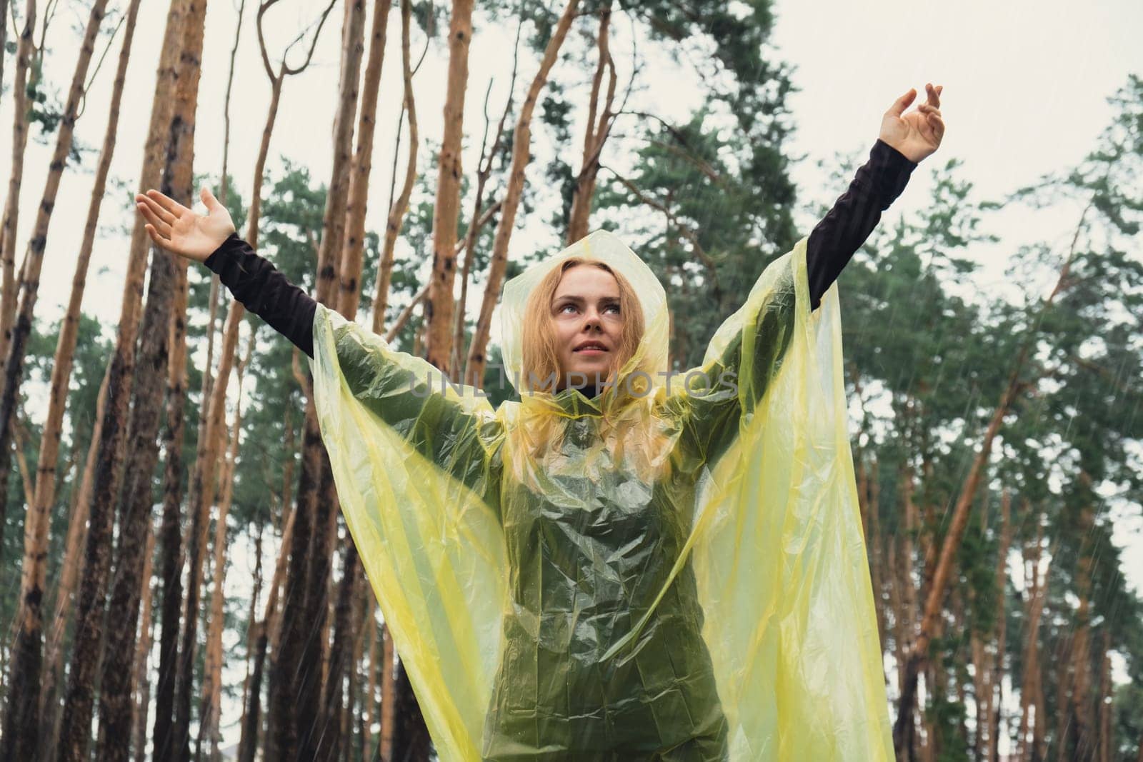 Smiling woman in yellow raincoat walking in autumn forest enjoying rainy weather outdoors. Female tourist discover park in rainy season. Closeness to nature. Mental healing fulfillment clean air